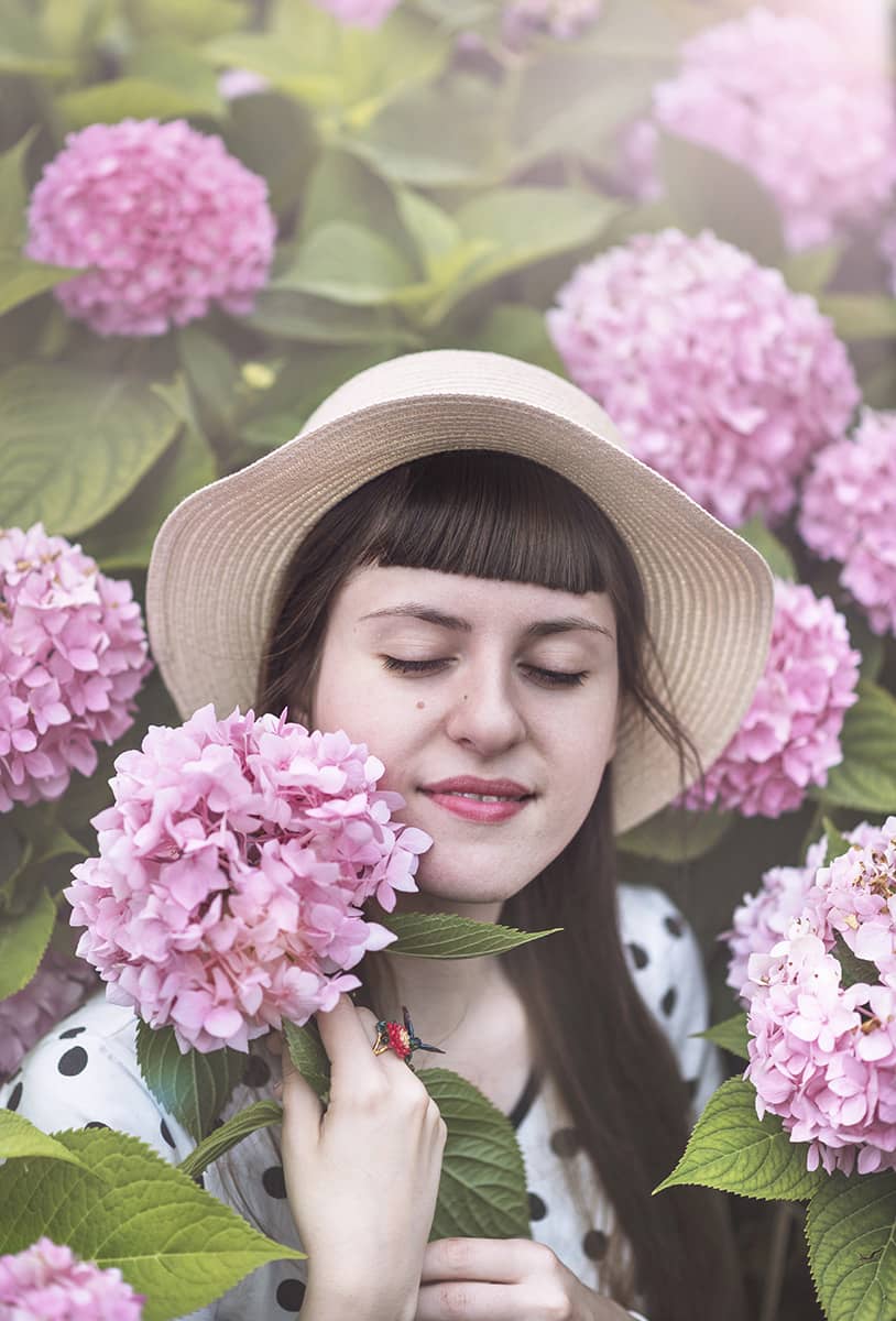 Nature-inspired hummingbird ring worn by a woman in a pink floral setting.