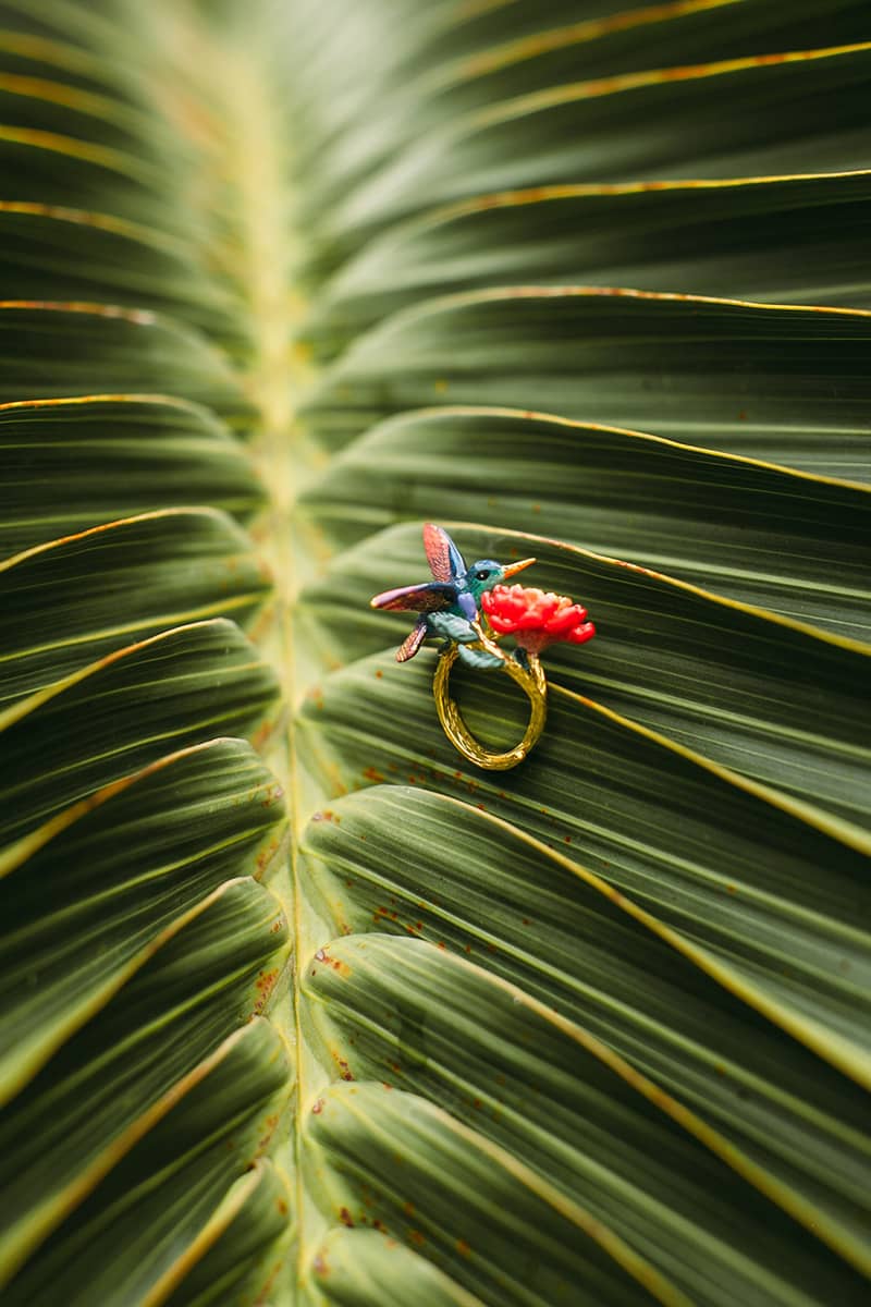 Nature-inspired hummingbird ring placed on palm leaves.