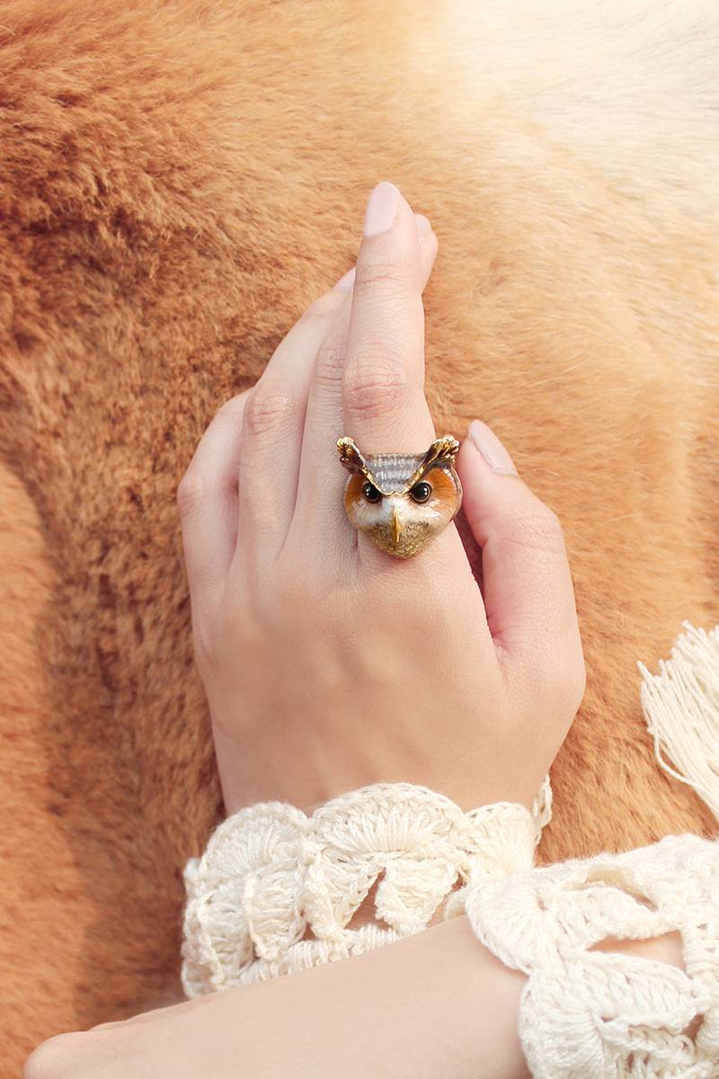 A hand wearing an adorable owl ring, with intricate crochet sleeve, rests on a soft, brown fur surface.