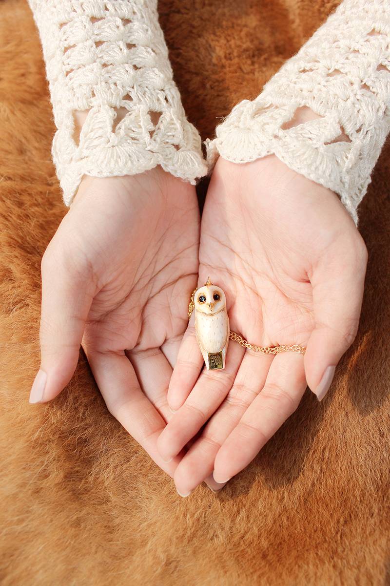 Hand holding a whimsical owl whistle necklace with a gold chain.