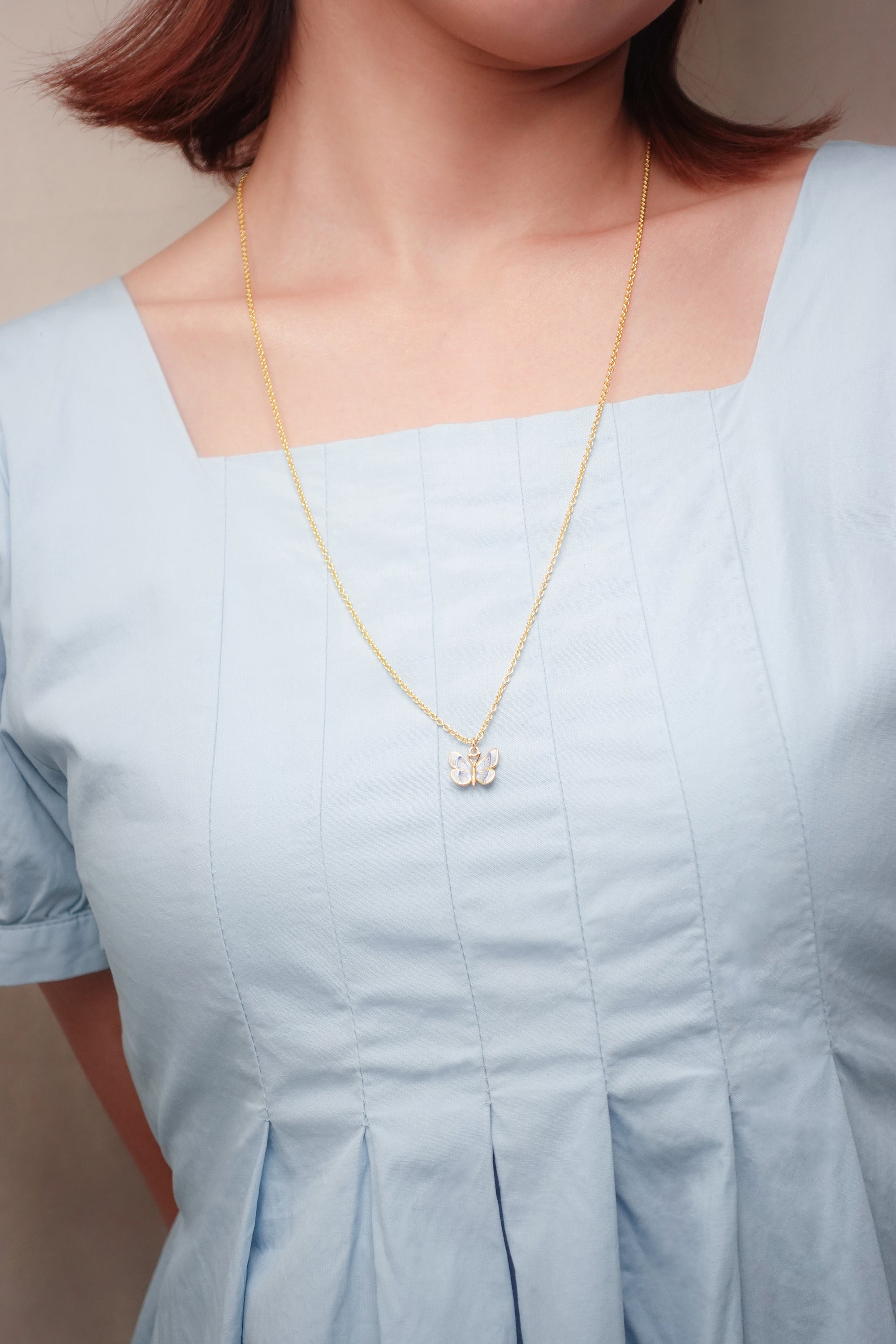 Close-up of a woman wearing a beautiful butterfly necklace on a blue dress.