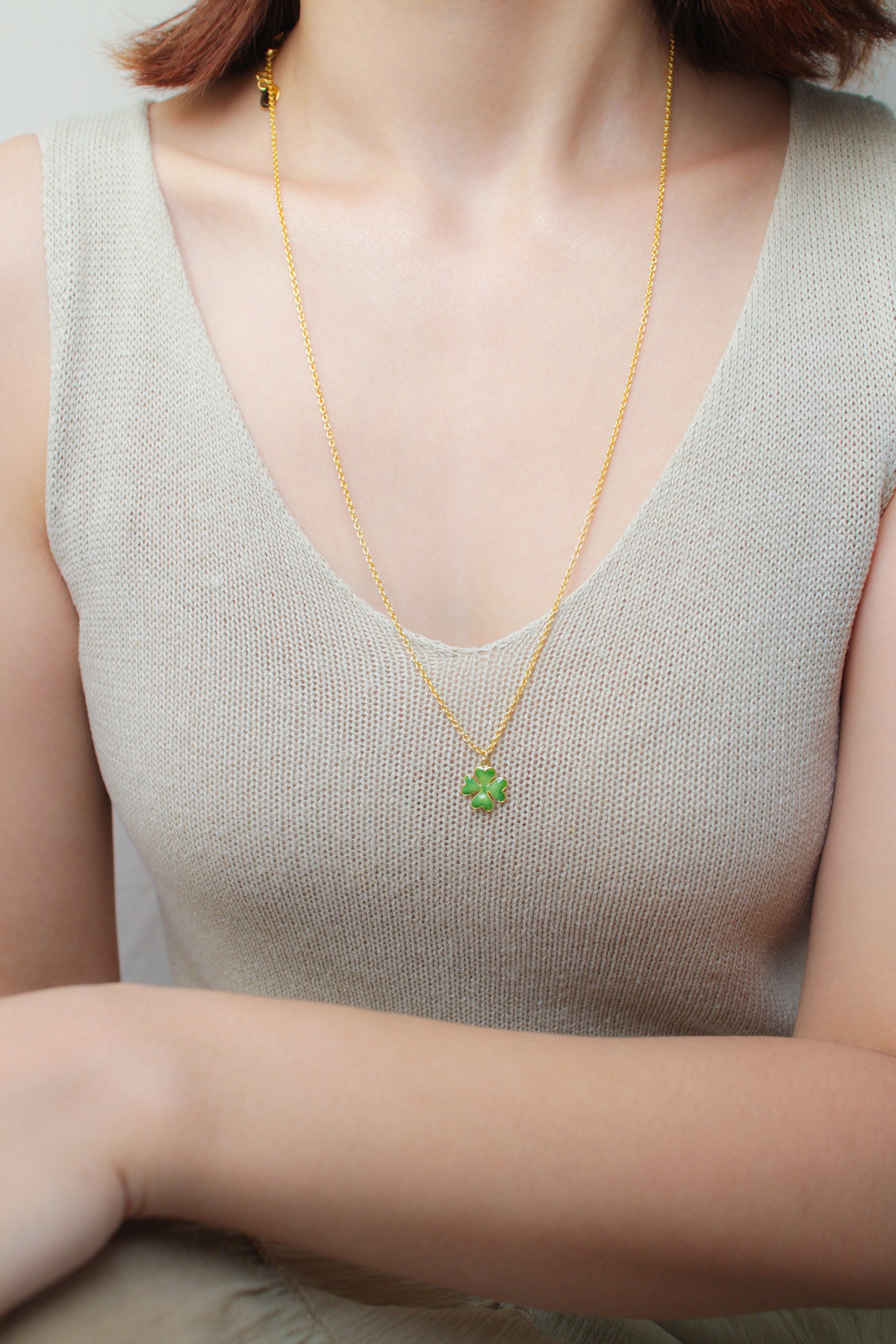 A close-up of a person wearing summer outfit, showcasing a gold chain necklace with a green clover pendant.