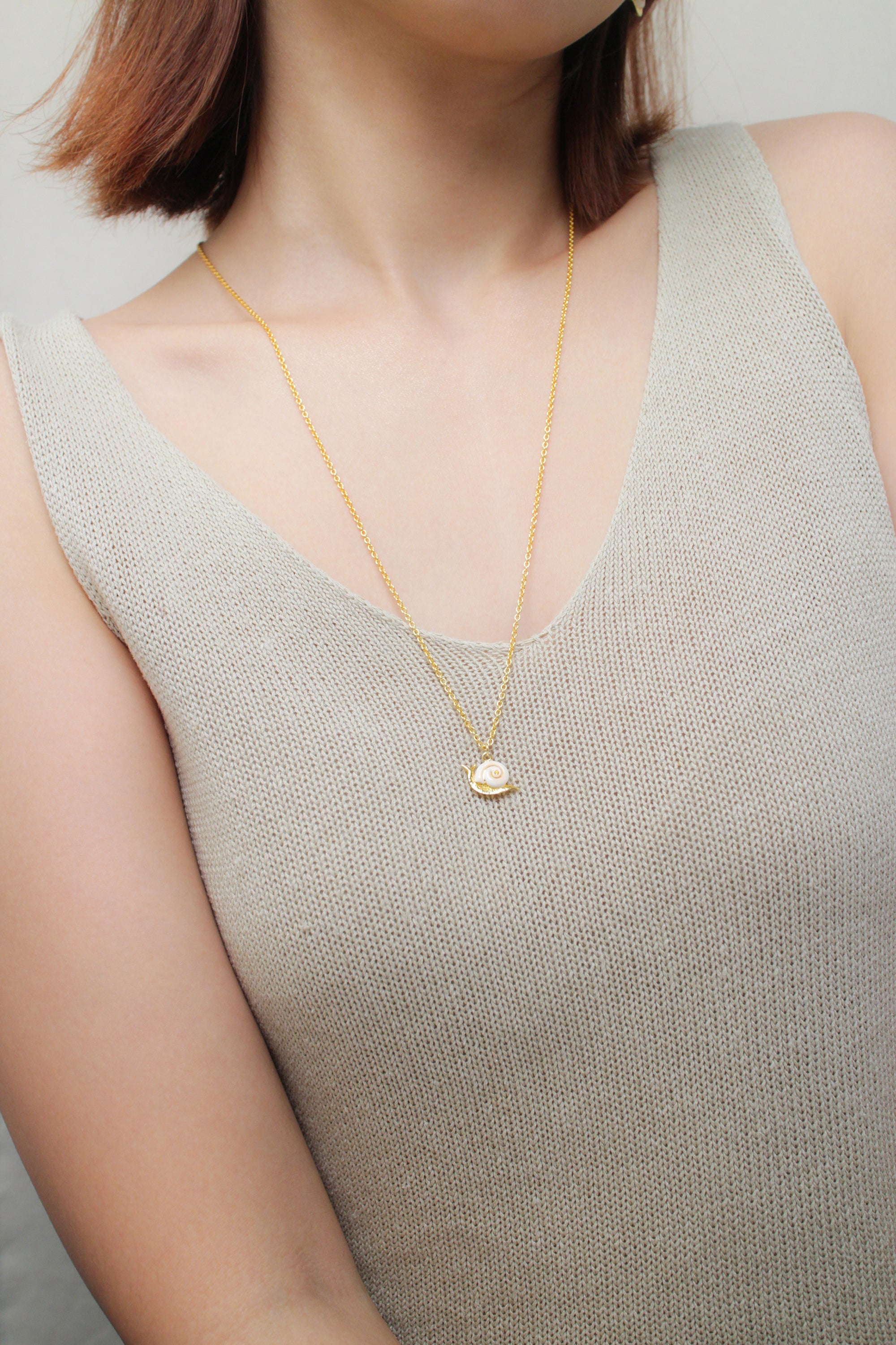 Close-up of a woman with summer outfit wearing a snail necklace.