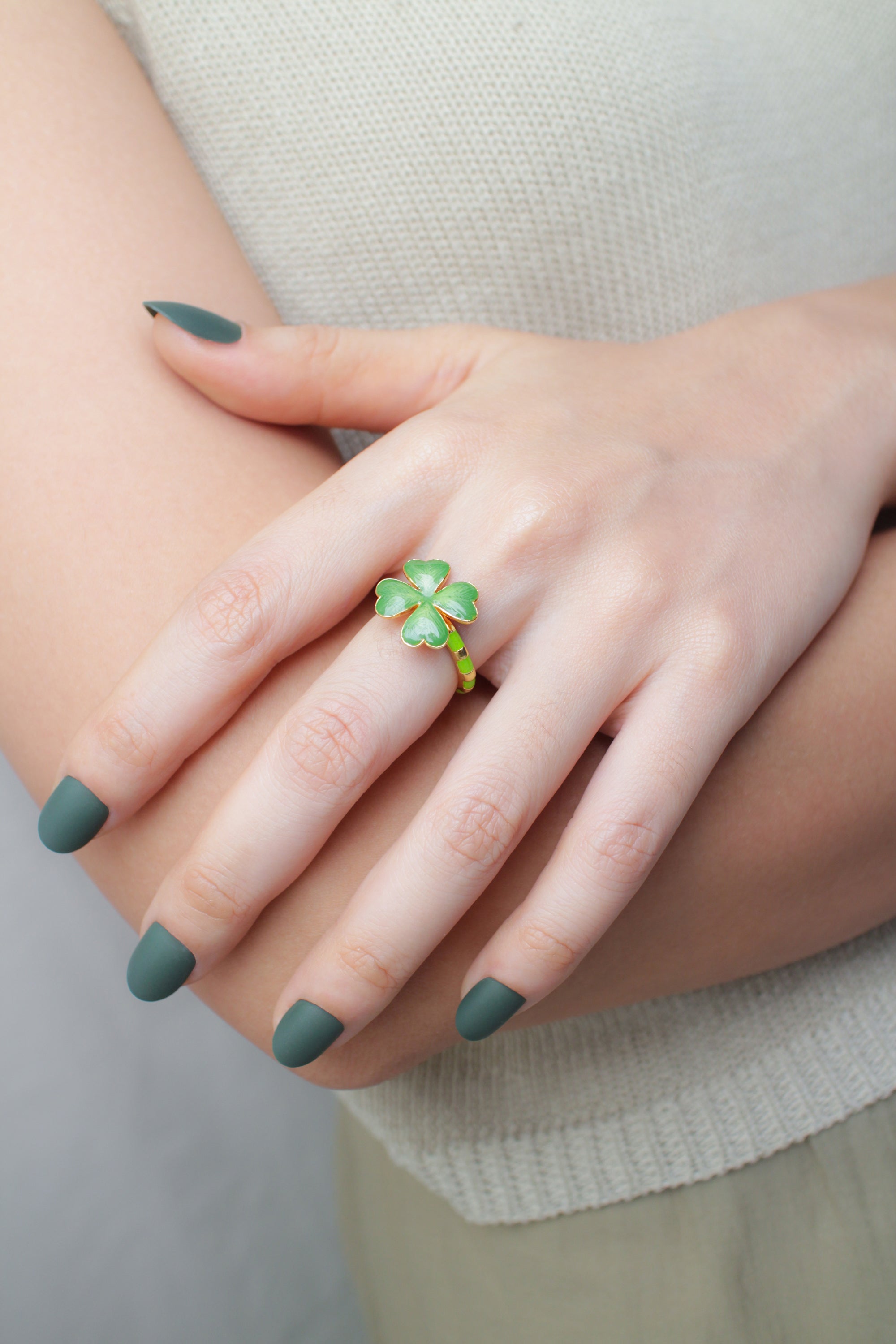 A hand with green nail polish displays a delicate green clover ring on its finger, with a summer outfit.