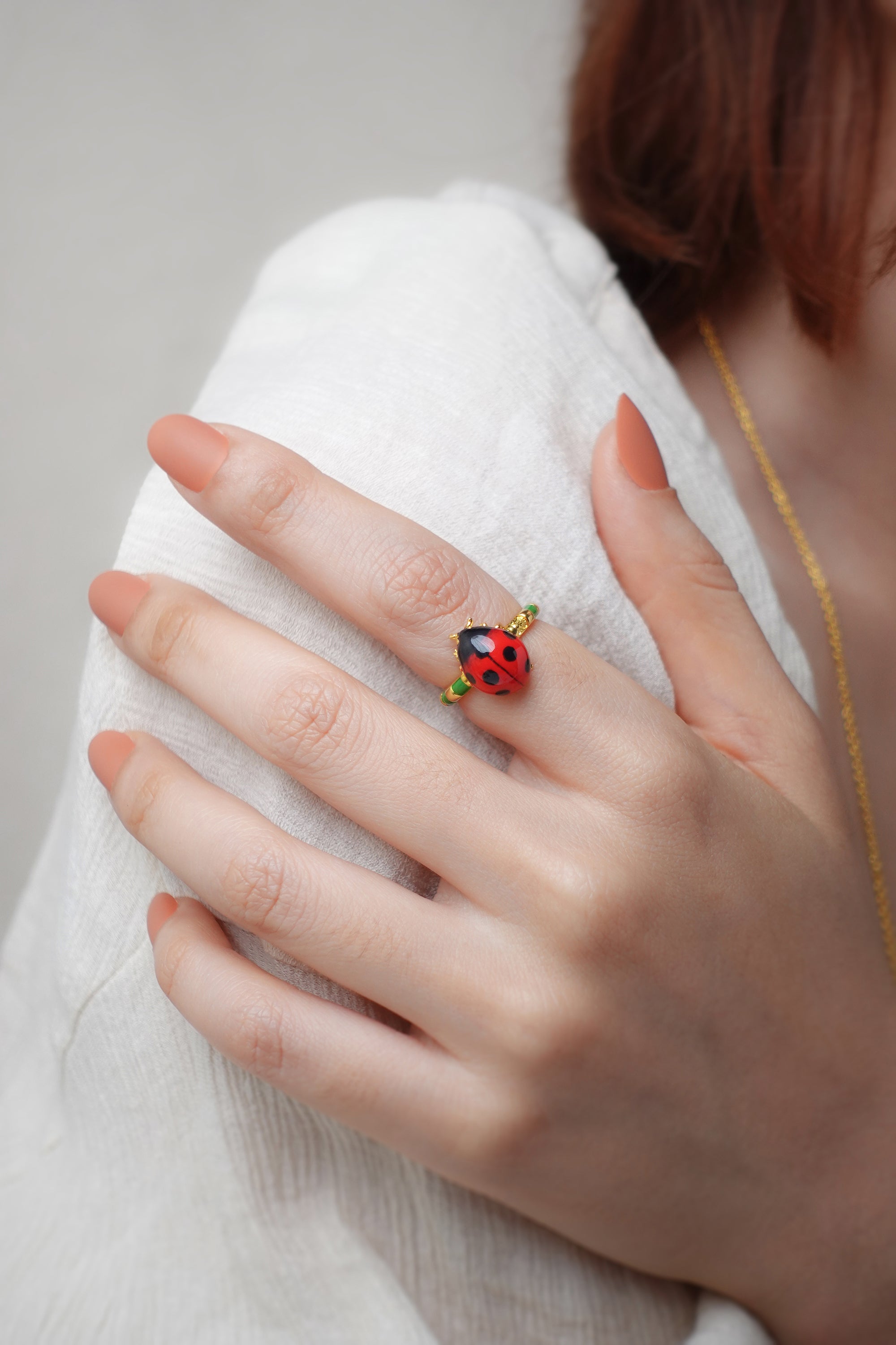 Close up of a hand wearing nature-inspired ring featuring red ladybug design