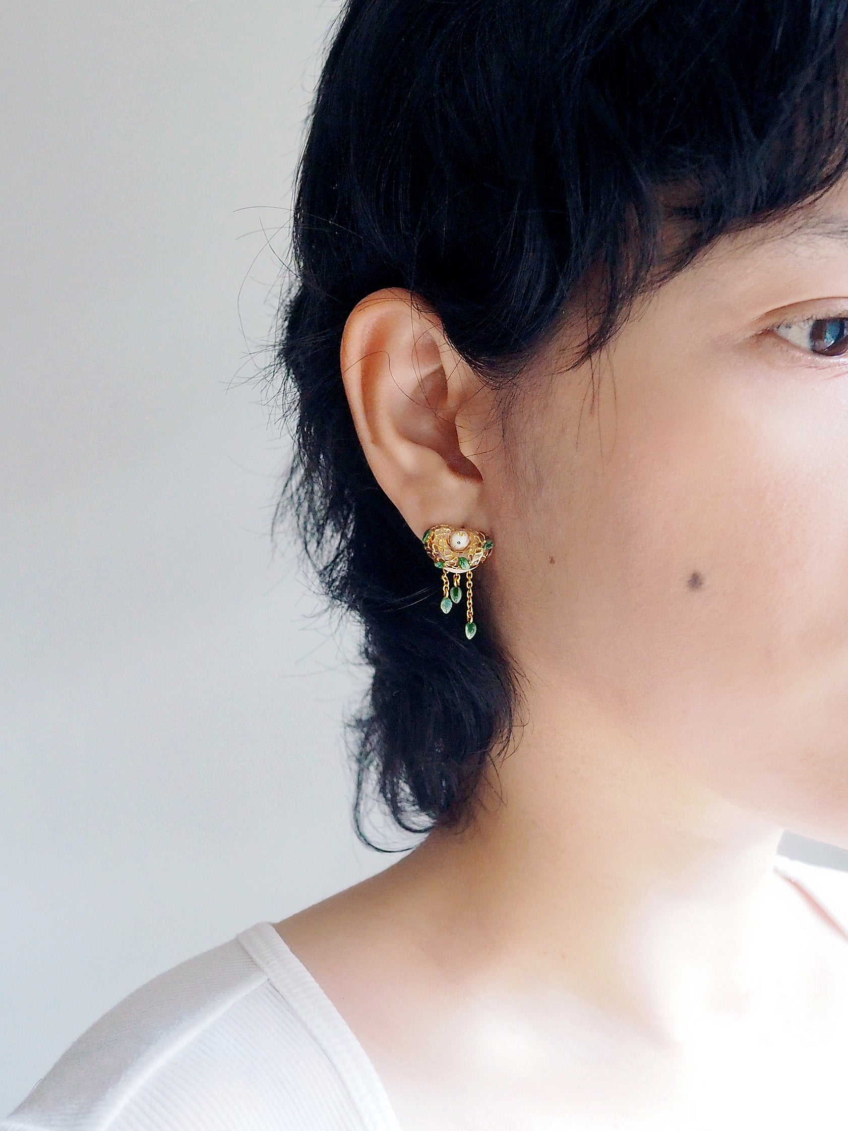 Woman wearing unique earring featuring a bird nest design.