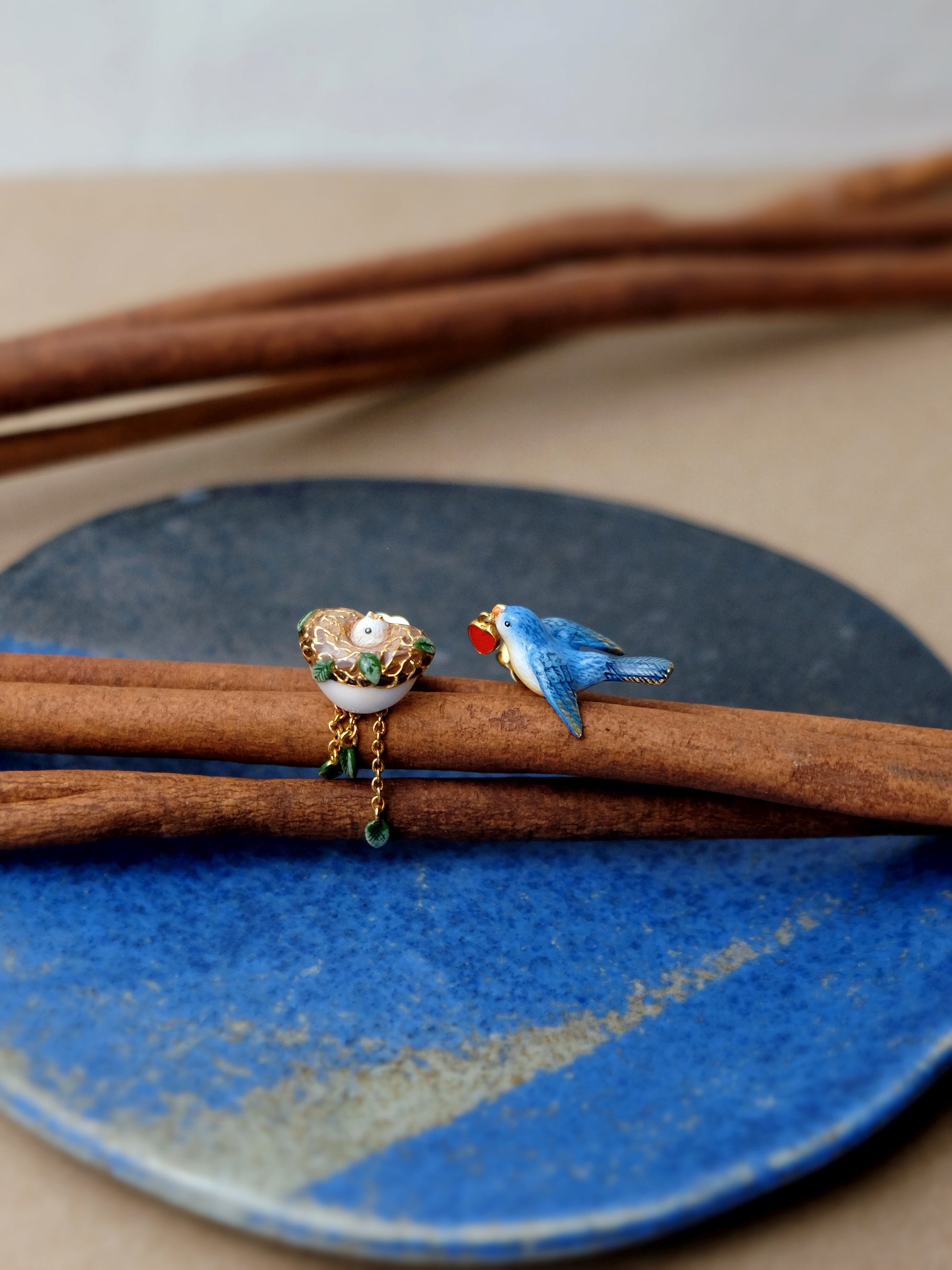 Colorful earrings featuring a bird, leaf and a nest designs, with gold accents and dangling elements.