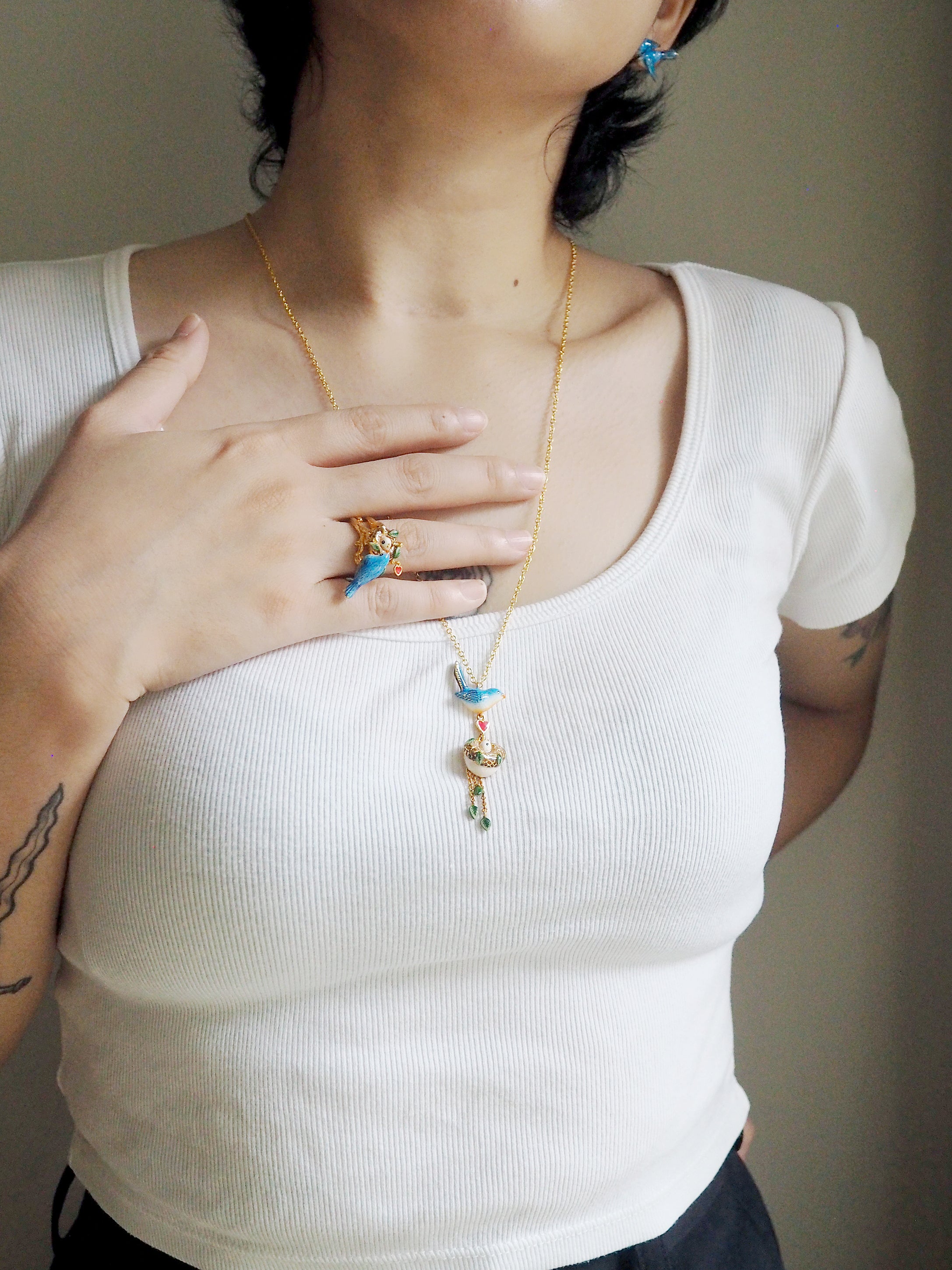 A model wearing a bird ring and a bird pendant necklace with a heart and nest charm