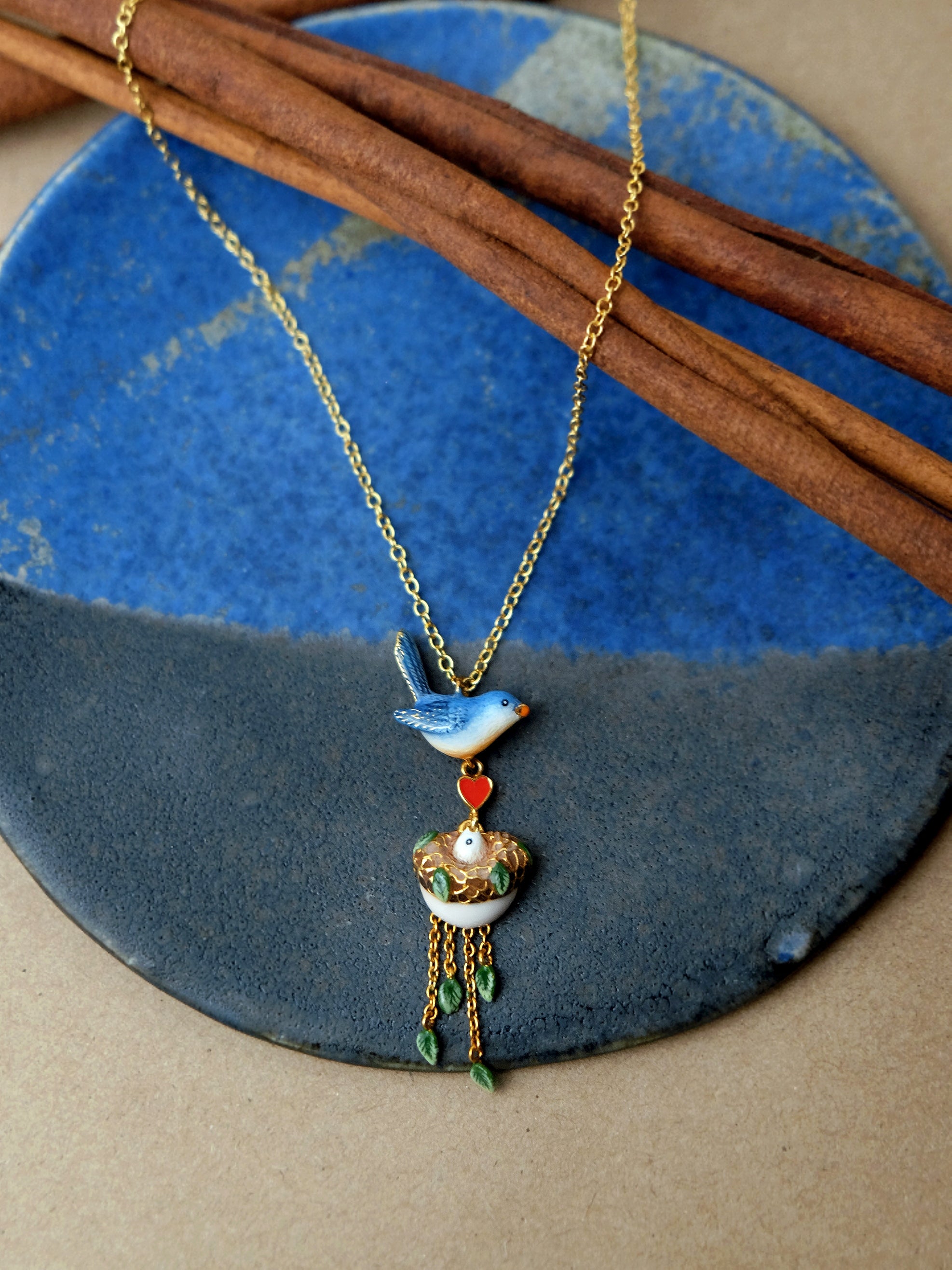 Beautifully crafted bird pendant necklace with a heart and nest charm place a plate.