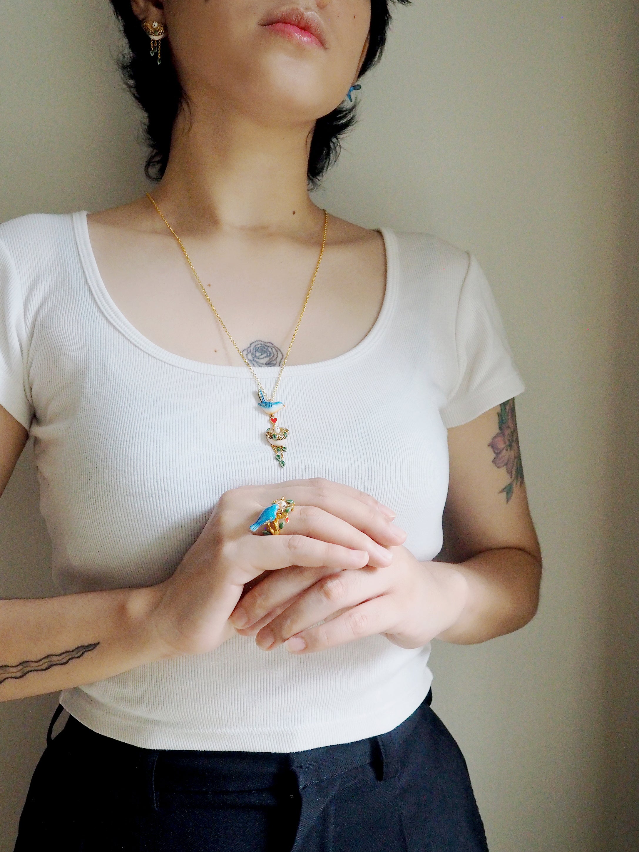 A model wearing a bird ring and a bird pendant necklace with a heart and nest charm