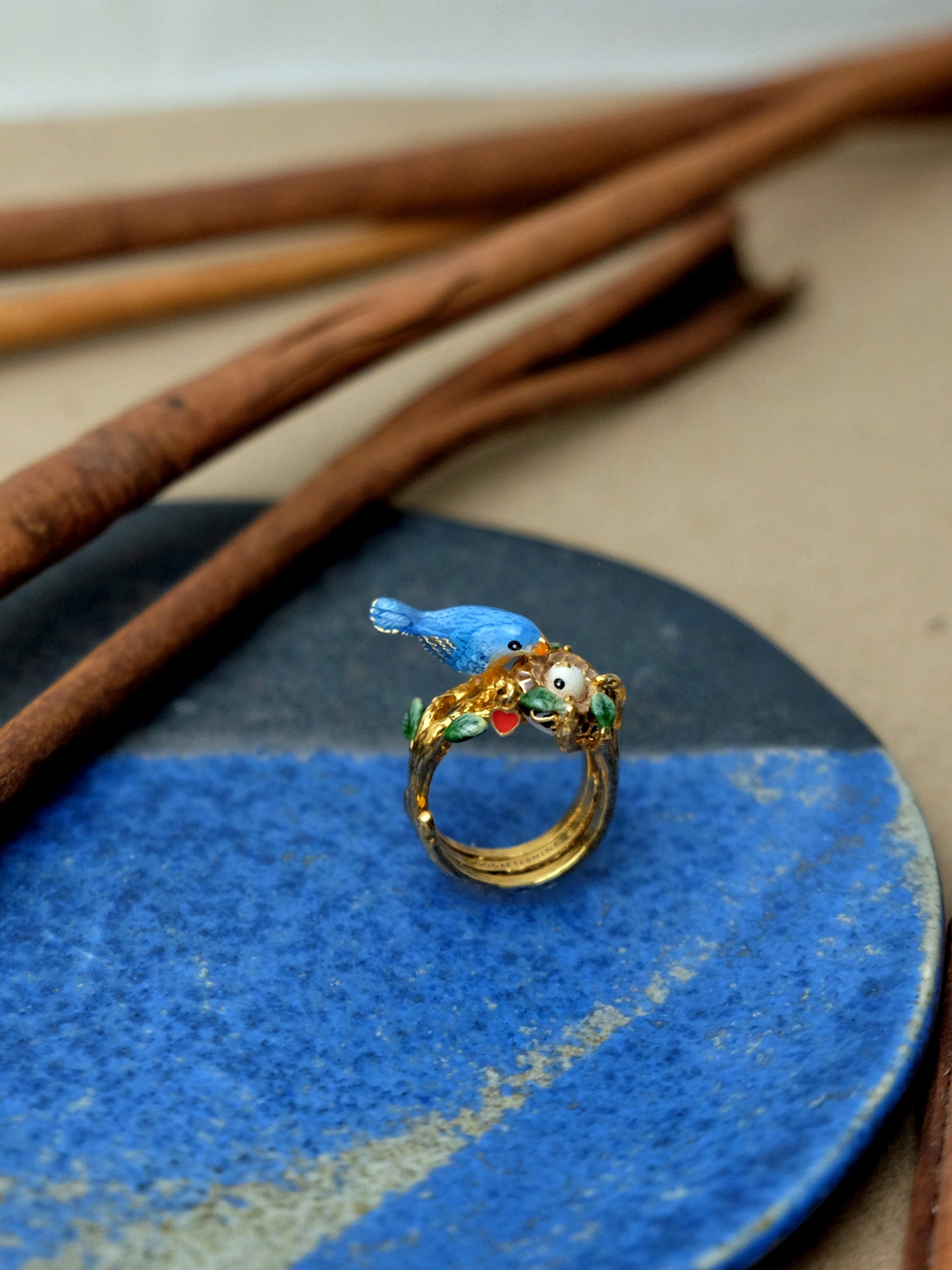 Beautifully crafted ring featuring a blue bird and baby bird in the nest design placed on a plate