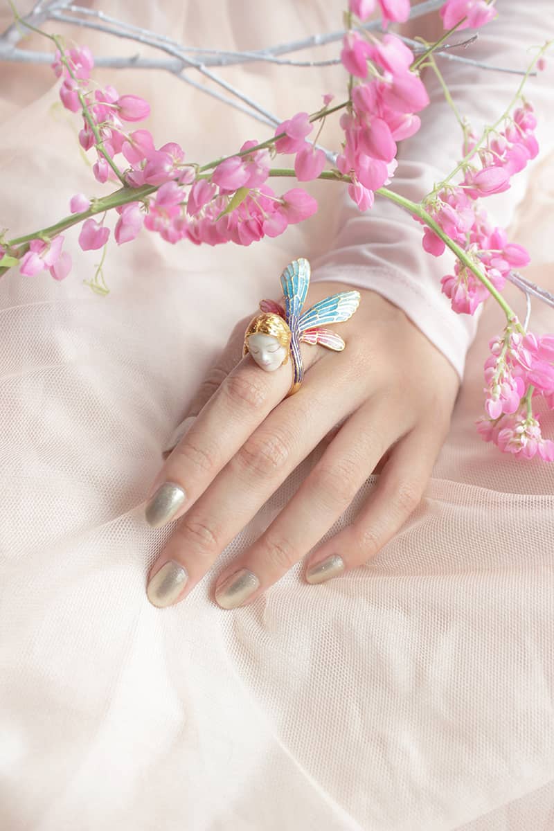 Close-up of a hand wearing a fairy ring surrounded by pink flowers