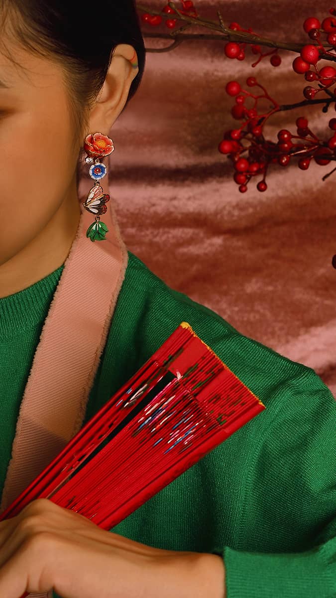 Close-up of a charming earring with colorful flowers, a butterfly and a leaf design worn on a model