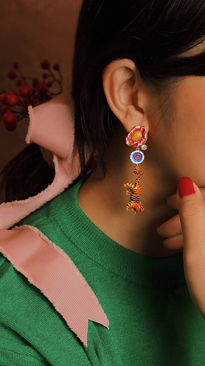 Colorful earrings featuring a floral design and a tiger hang from a woman's ear, complemented by a green sweater.