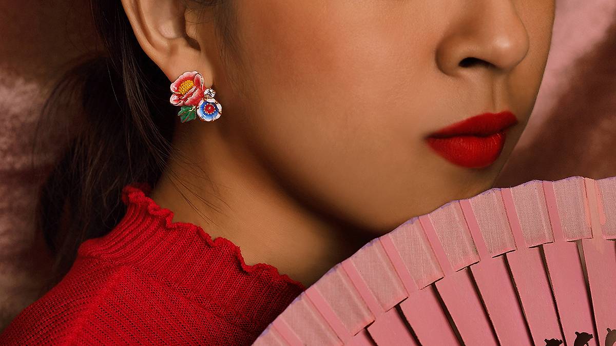 A close-up of a woman's ear adorned with colorful floral earrings, complemented by a pink fan nearby.