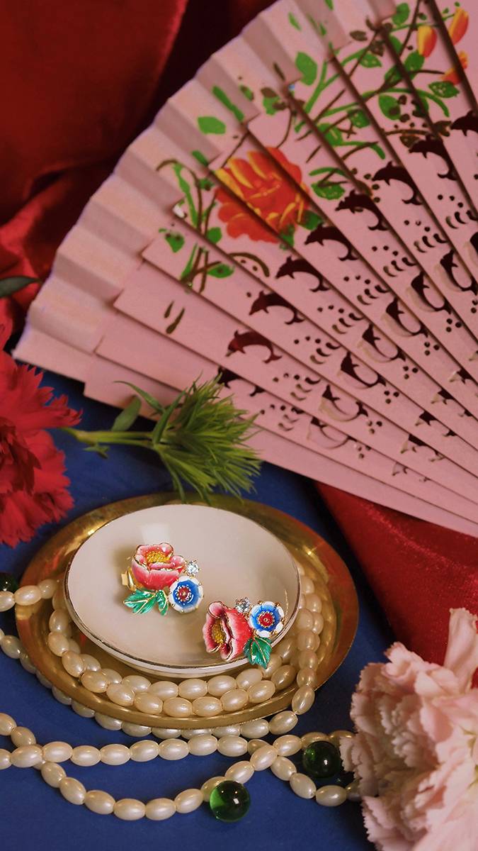 A beautiful floral earrings, a pearl necklace, and a decorative fan set against blue and red fabrics.