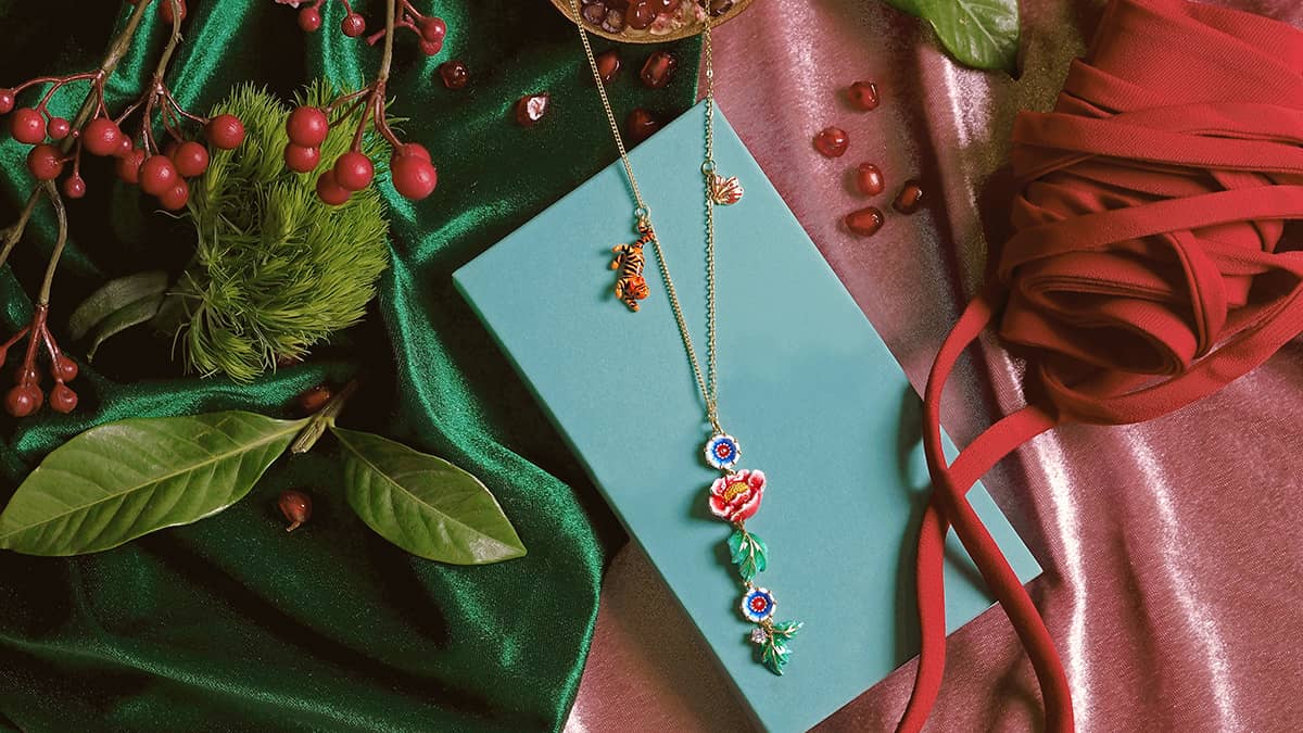 Unique necklace featuring floral and animal motifs displayed on a teal box amidst decorative elements and fabric.