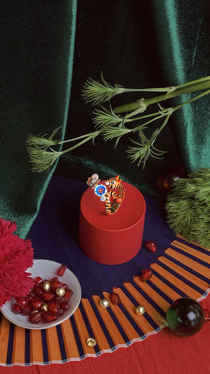 Beautiful tiger ring with a butterfly and a flower design on a red pedestal surrounded by flowers and pomegranate seeds.