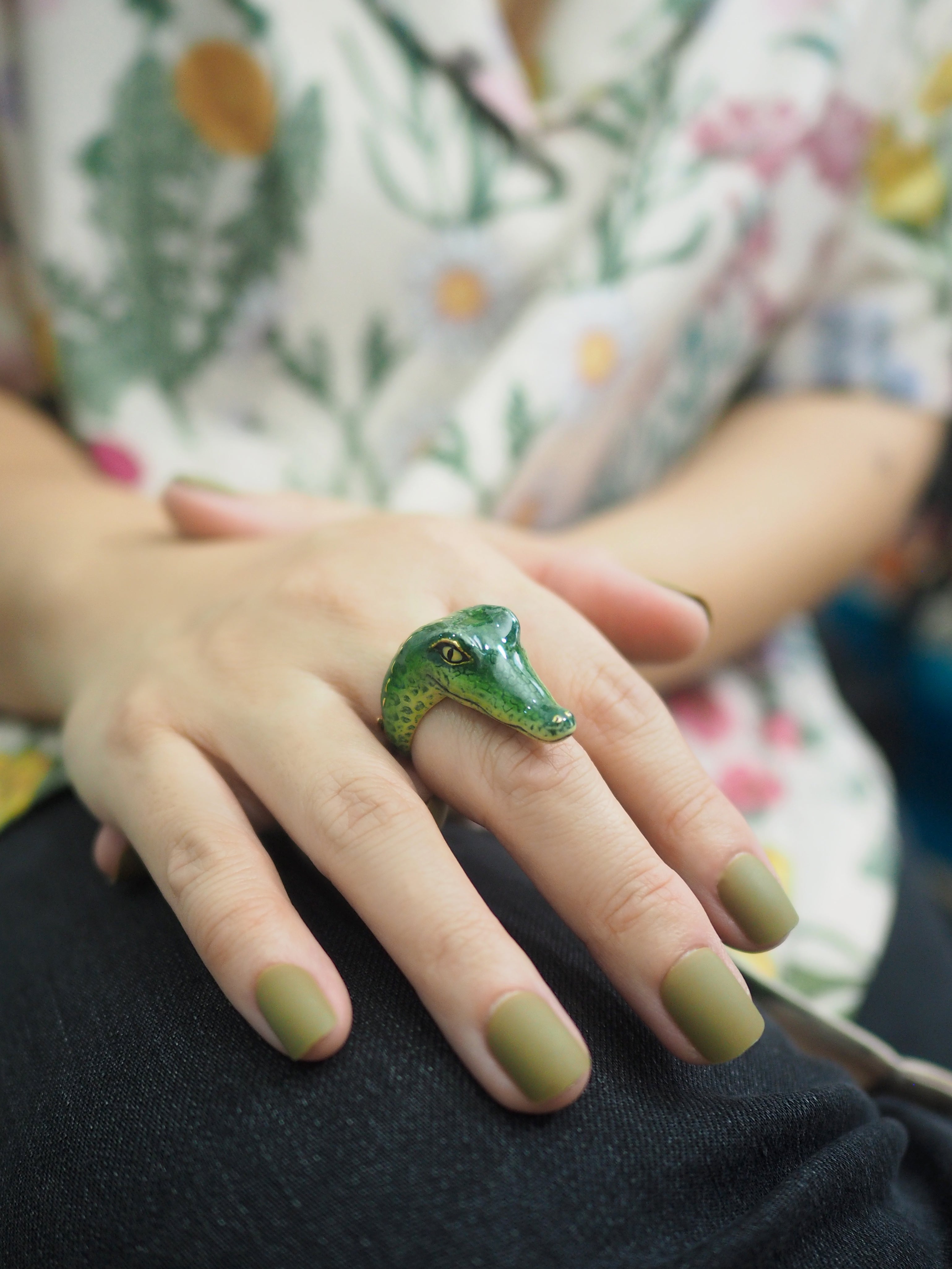 Detailed view of a crocodile ring worn on a hand with olive green nails.