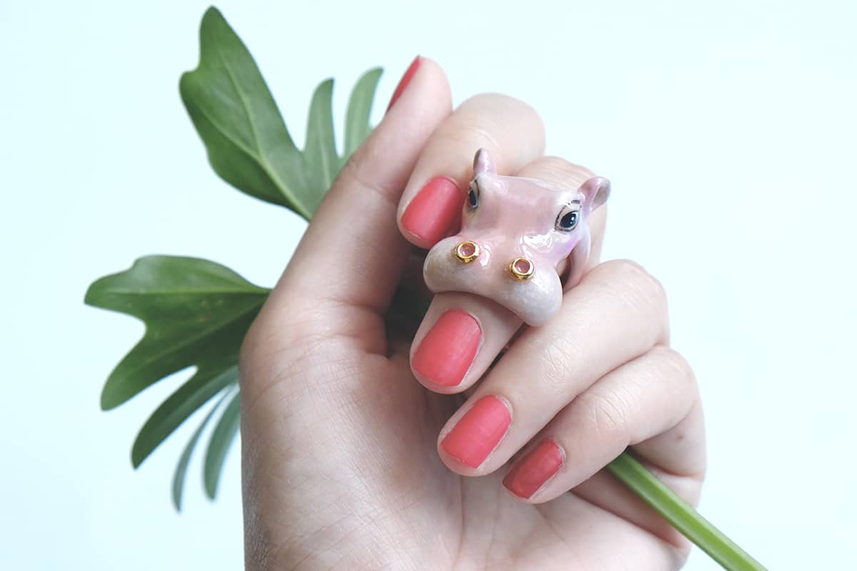 Playful hippo ring displayed on a hand with bright pink nails and green leaves, perfect for animal lovers.