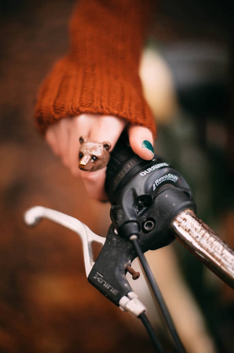 A person wearing an orange sweater holds a bicycle handlebar with a bear-shaped ring.