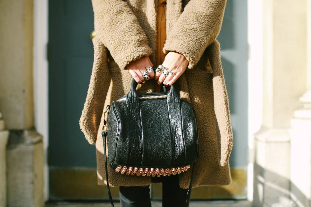 A woman holding a black handbag while wearing multiple skull rings on her fingers.