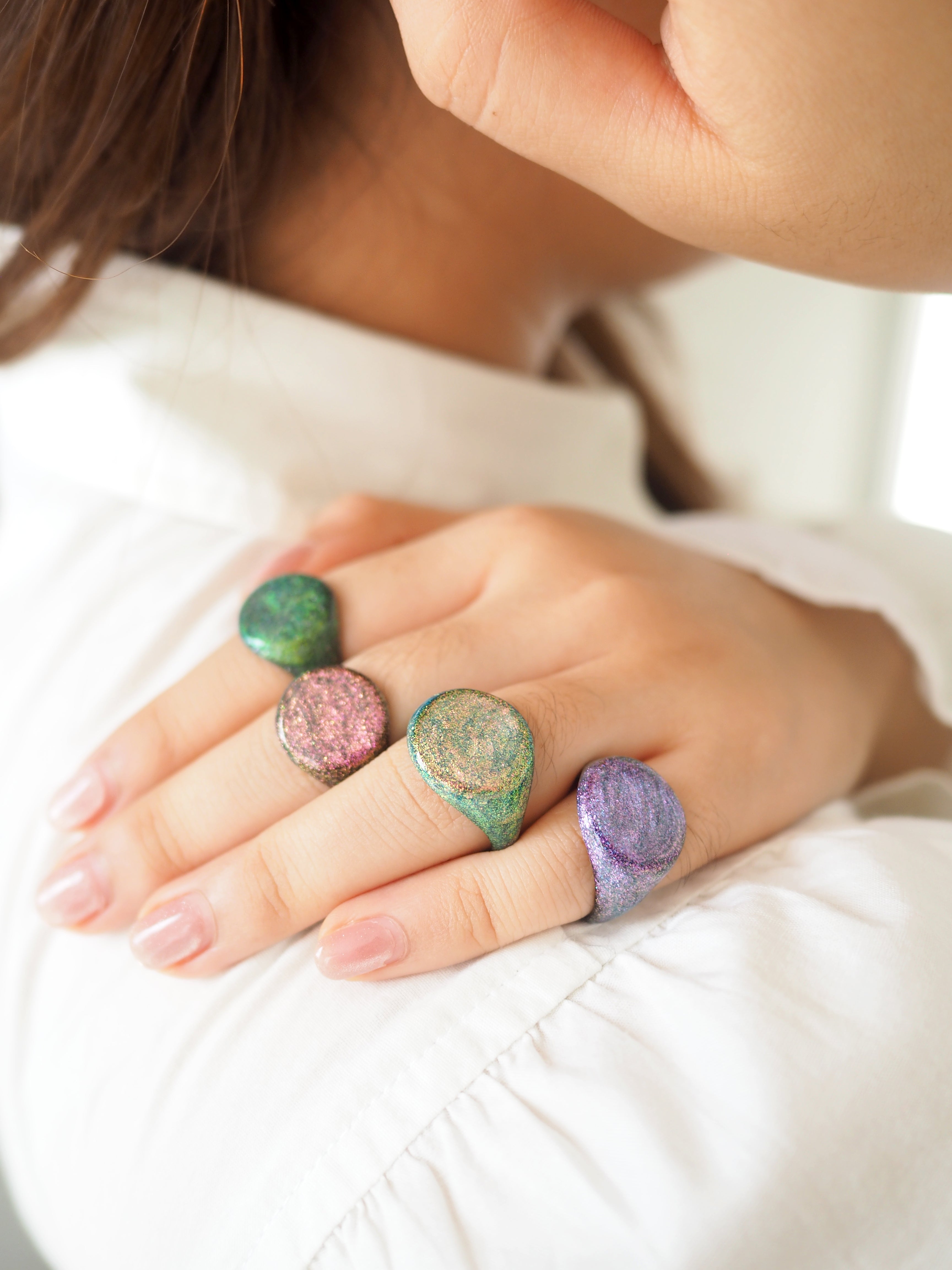 A close-up of a hand adorned with sky-inspired shimmer enamel rings in various colors.