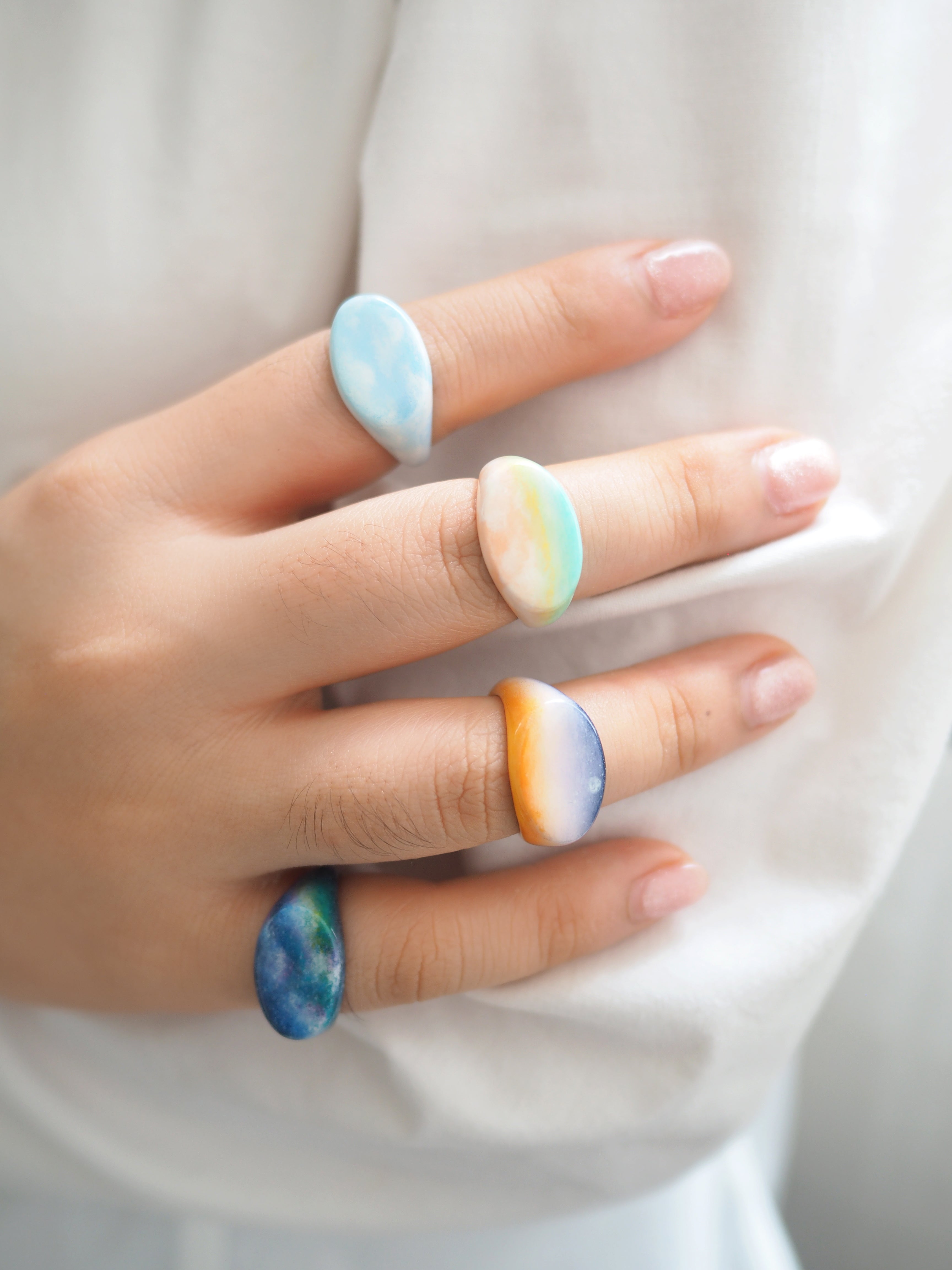 Unique hand-painted rings showcasing sky colors worn on a hand.