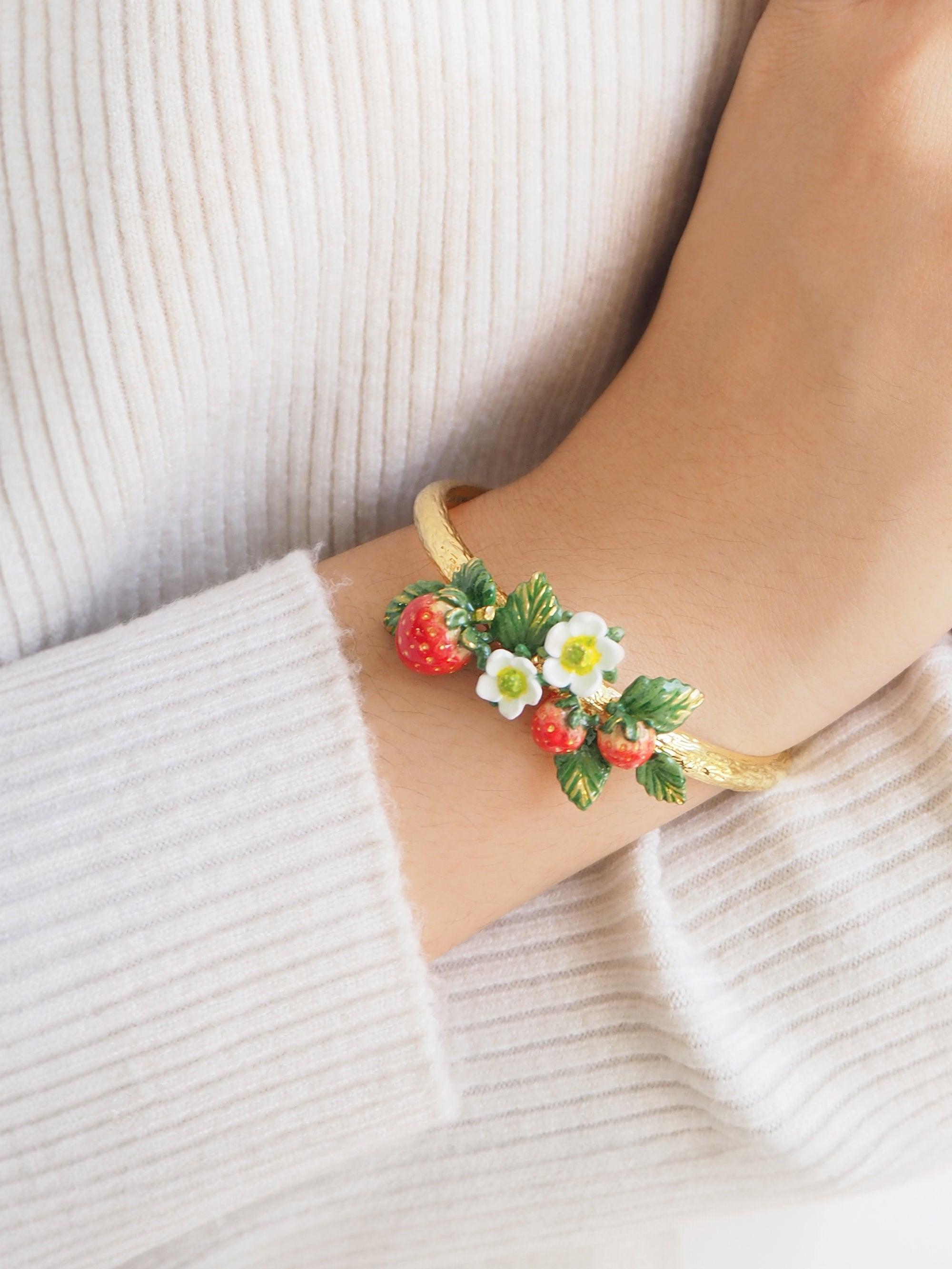 Close-up of a strawberry bangle adorned with white flowers and green leaves worn on a person's wrist.