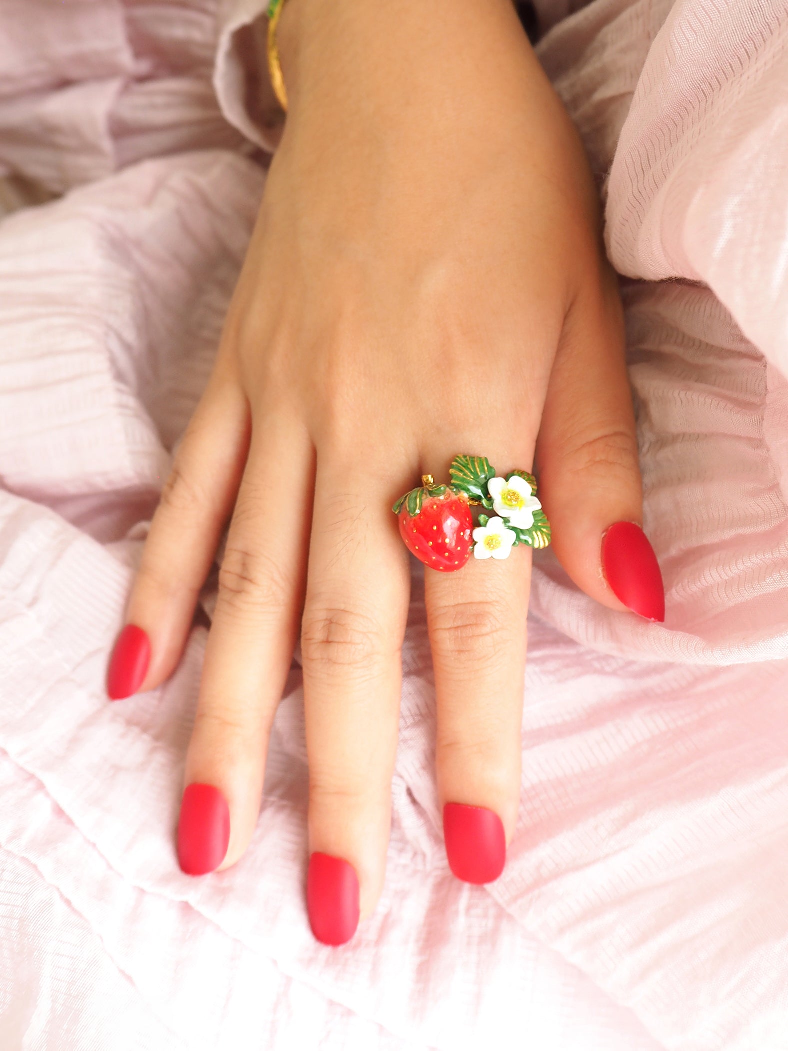 Close-up of a hand with red nails wearing a light pink dress and a floral strawberry ring