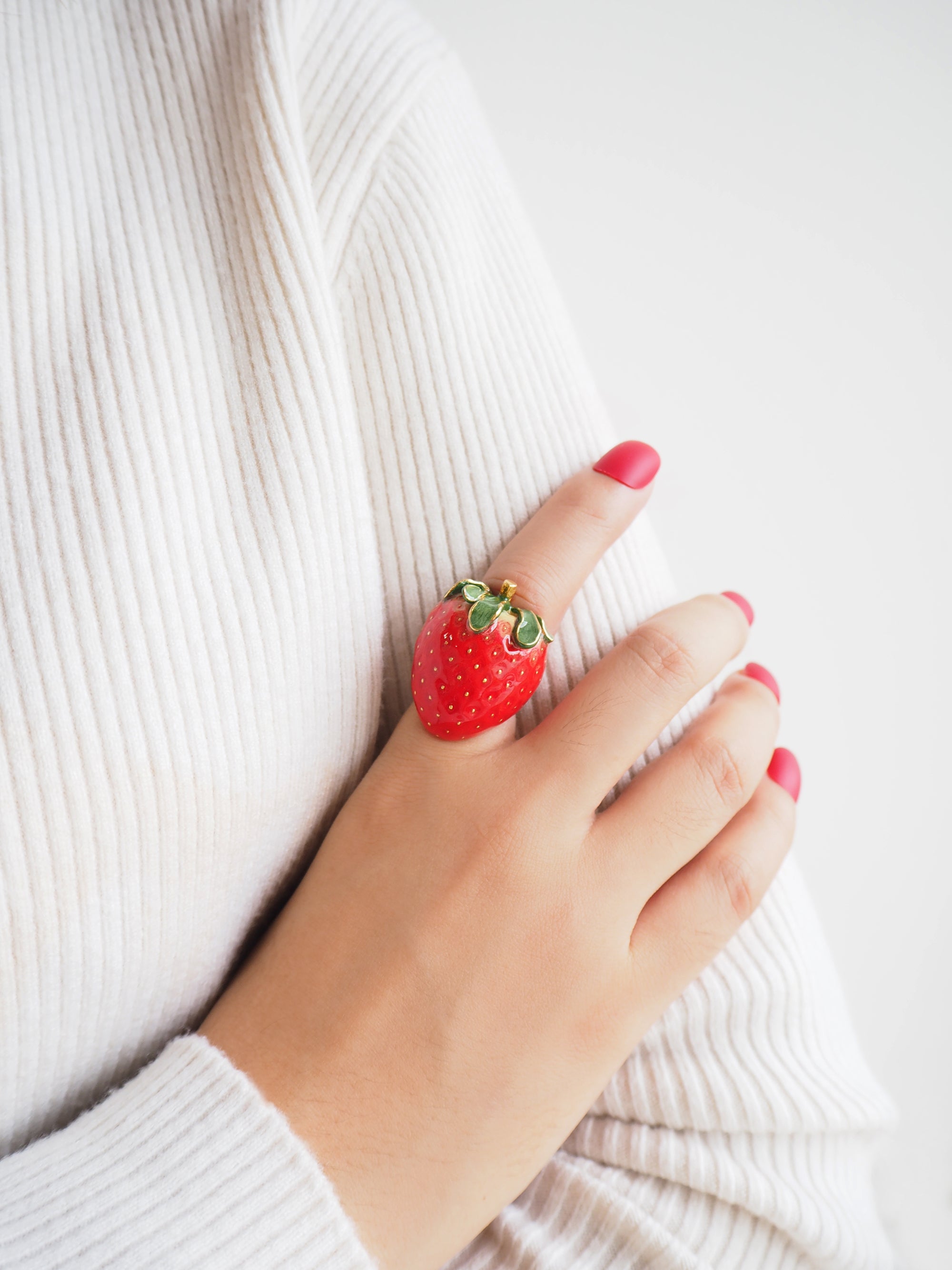 Close-up of a hand with red nails polish wearing a red strawberry ring