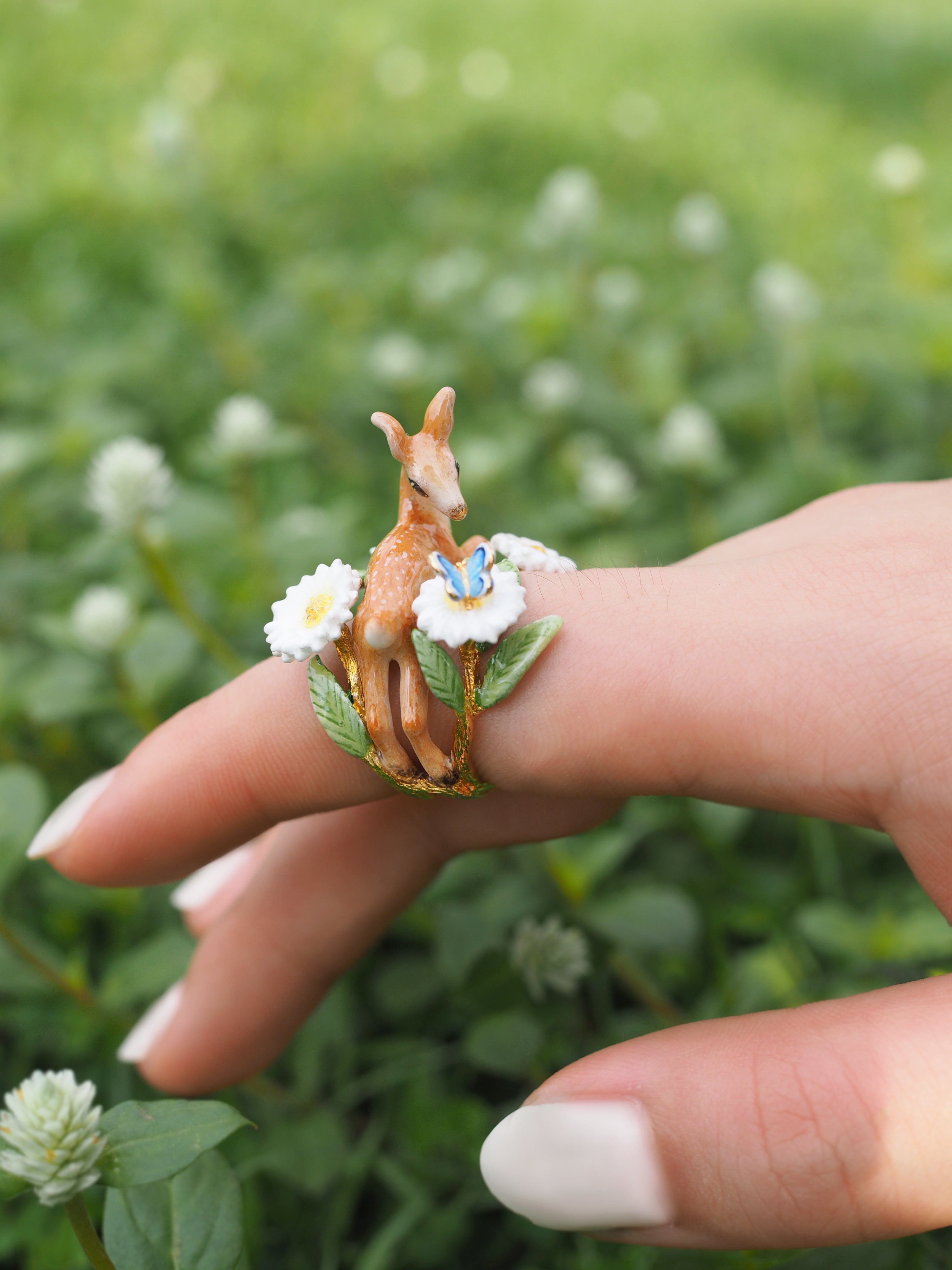 A nature-themed ring with a deer and floral design, photographed in a lush green environment.