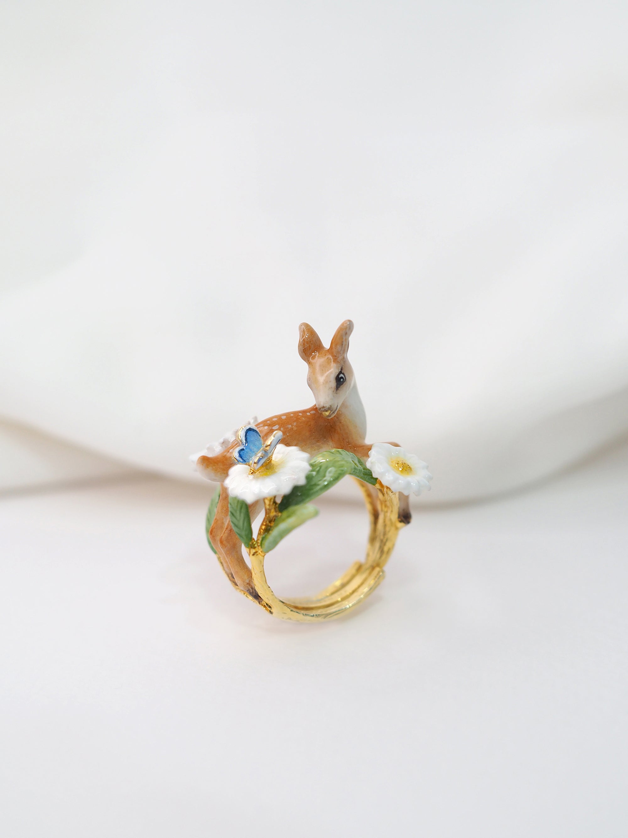 A beautifully crafted ring featuring a deer, a butterfly and floral placed on a white background.