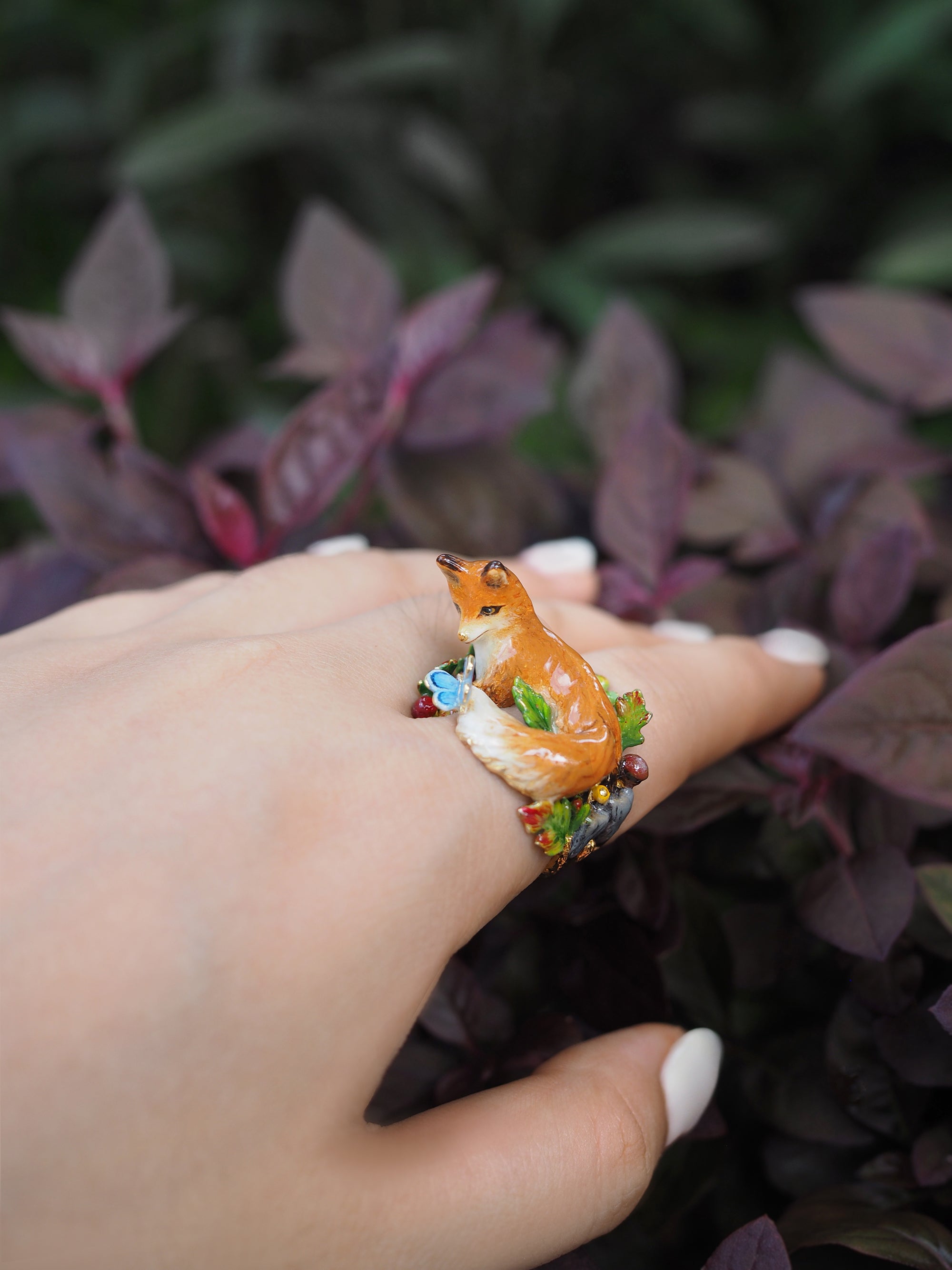 Artistic ring featuring a fox and decorative elements, displayed on a hand in a natural setting.