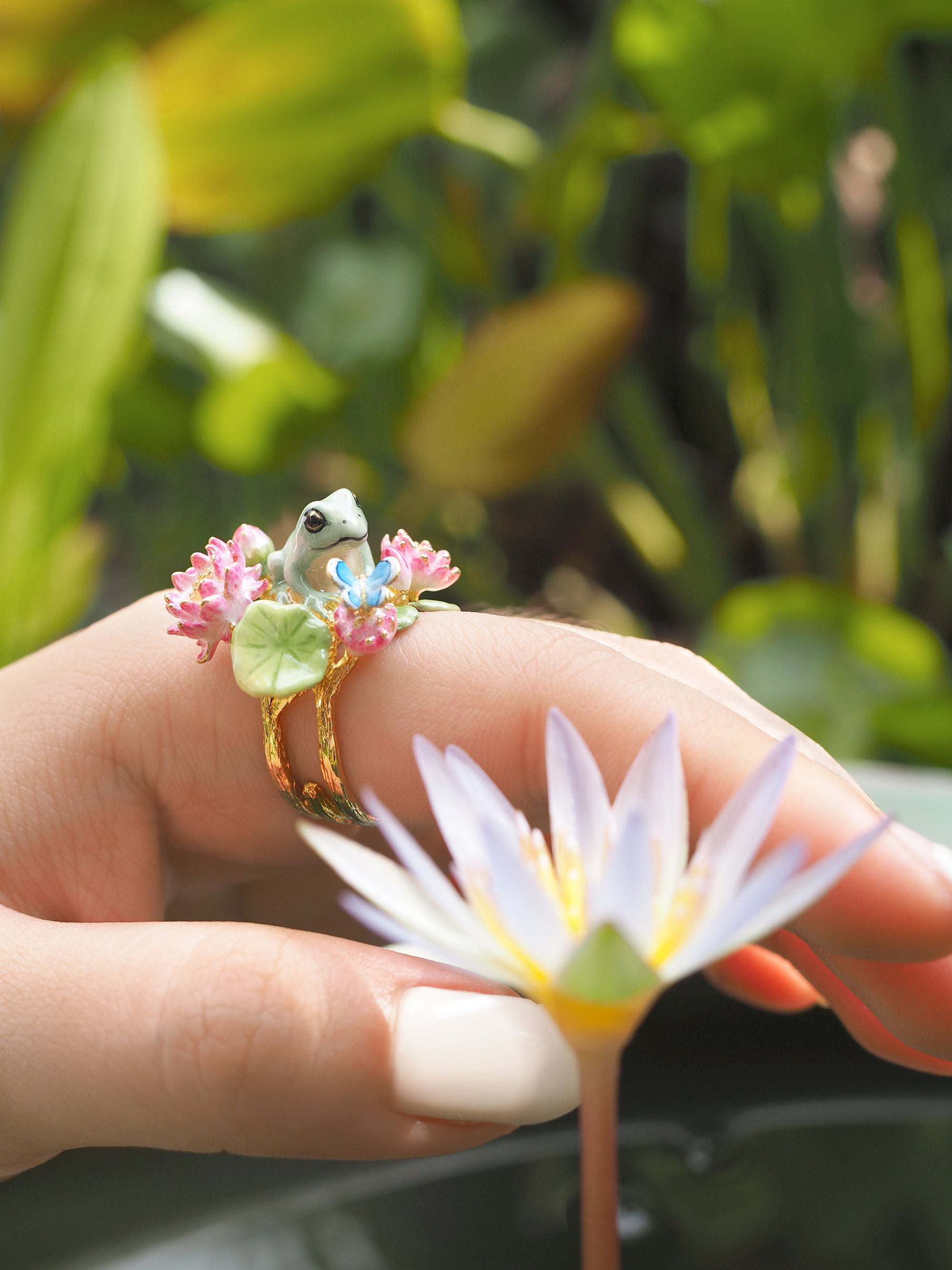 close up of a hand wearing a unique handcrafted ring showcasing a frog surrounded by pink flowers.