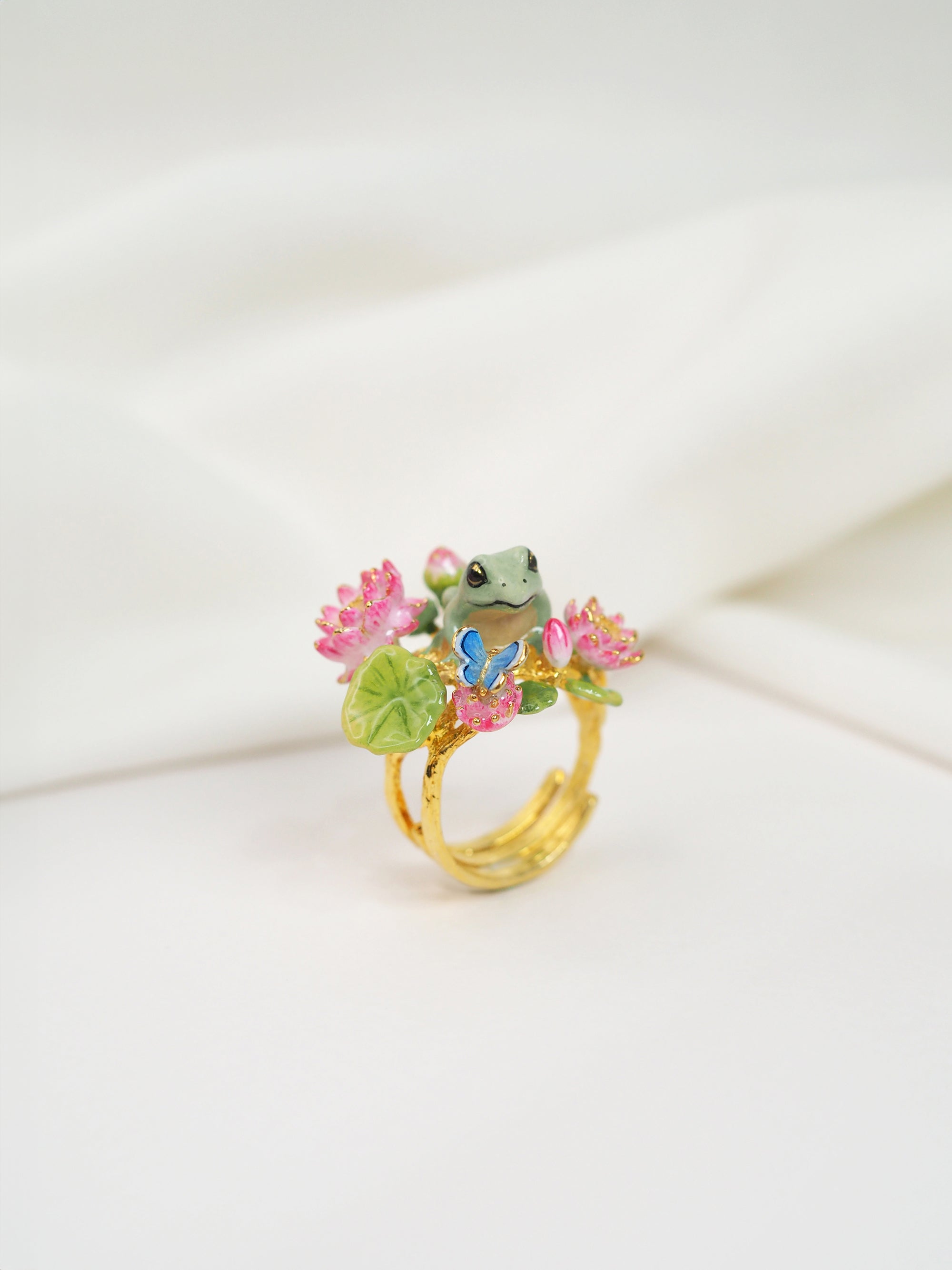 Artistic gold ring with a detailed frog and vibrant floral design placed on white fabric.