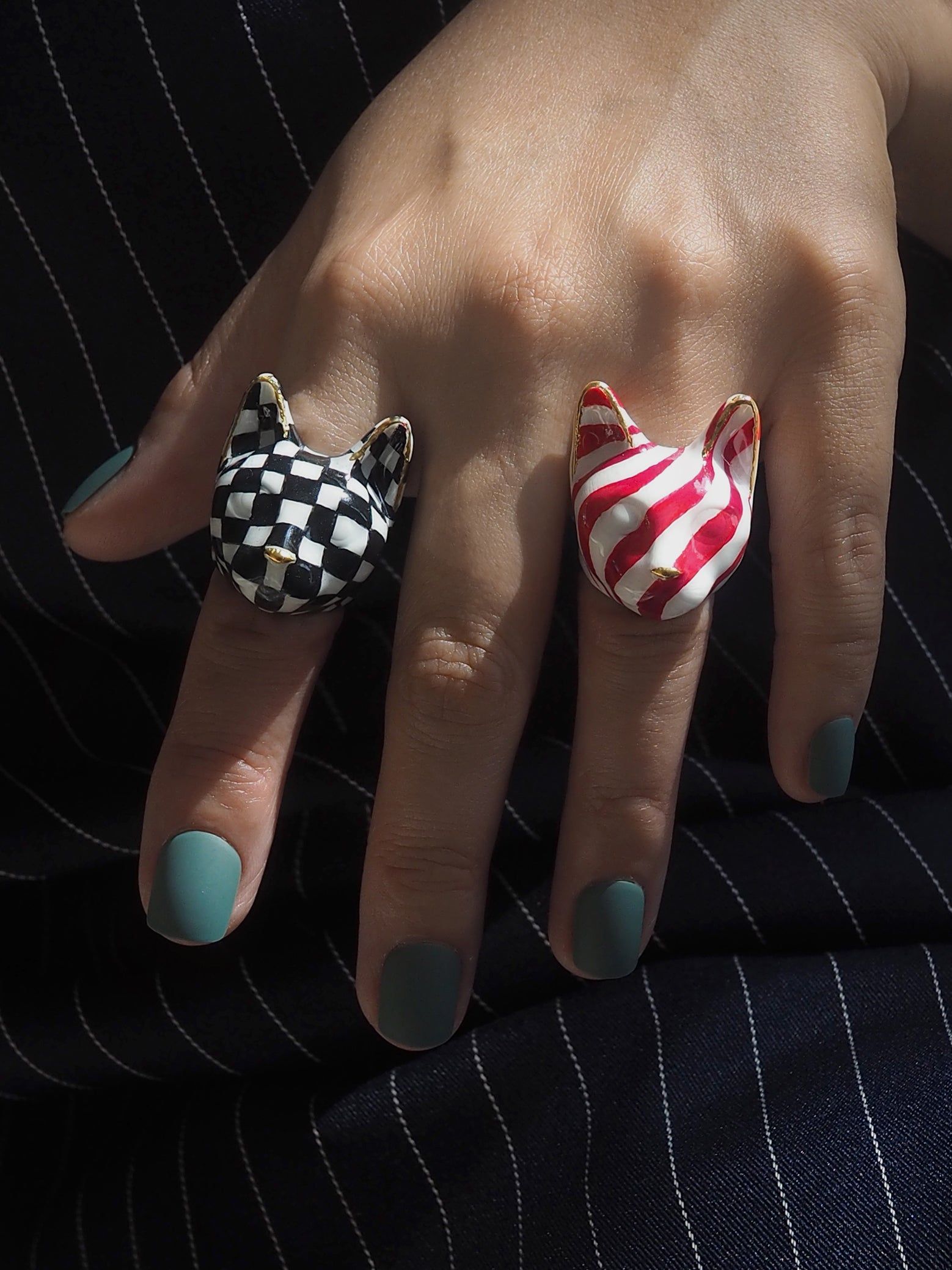 Close-up of a hand wearing cat rings, one striped red and white and the other in a black and white checkered pattern.