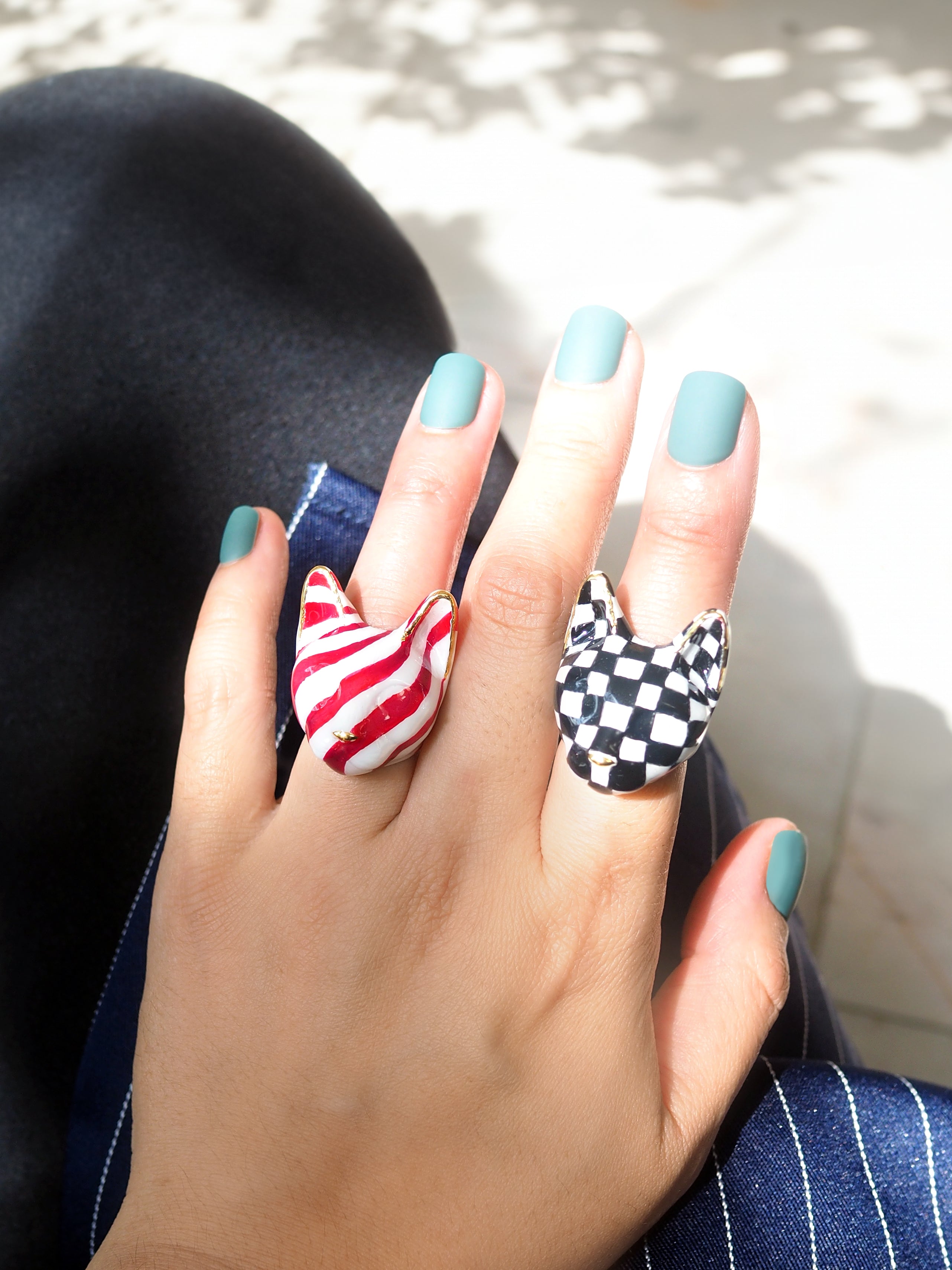 Close-up of stylish cat rings on a hand with teal nail polish.