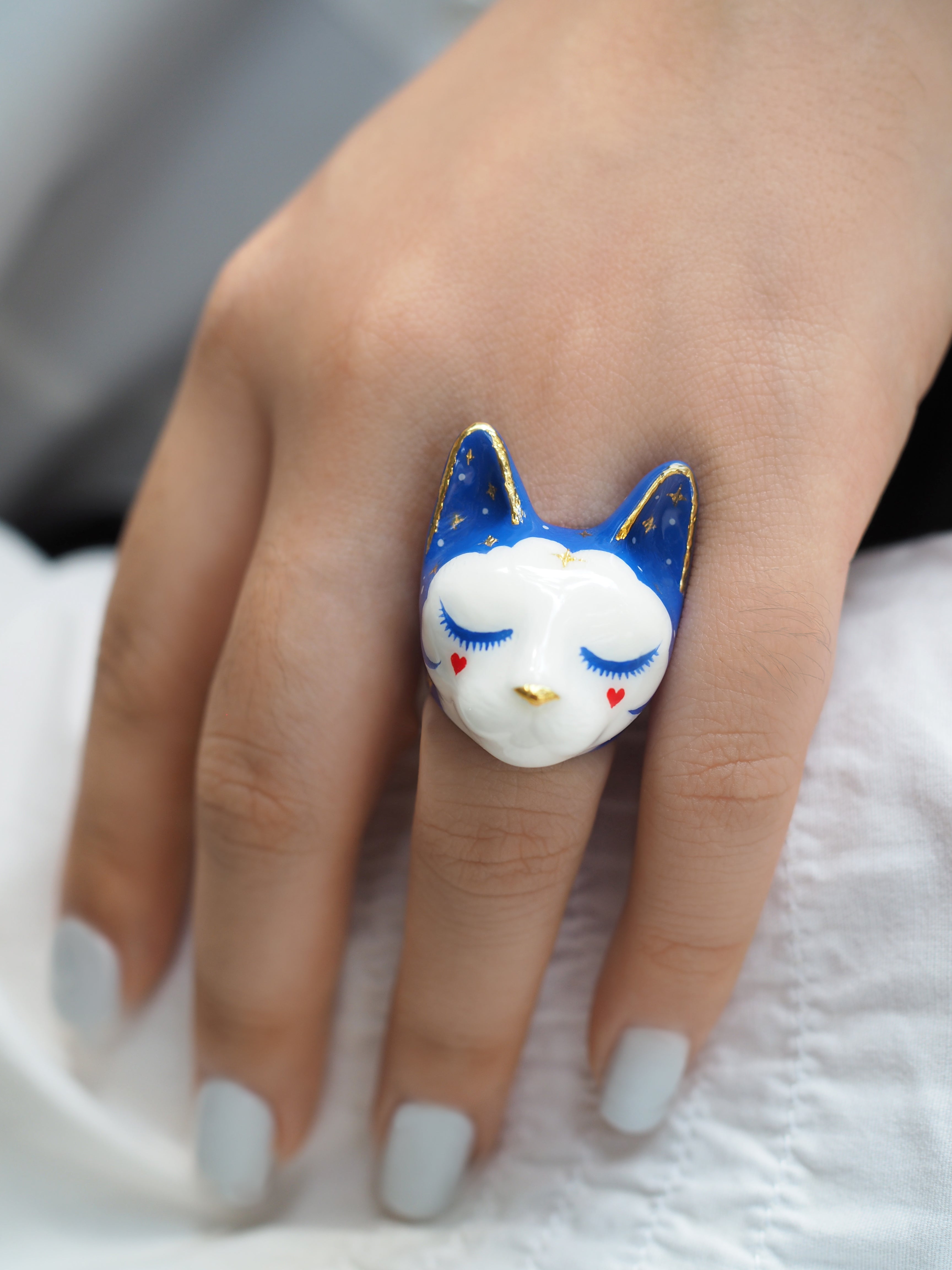 Close-up of a whimsical cat ring featuring a blue design and cute facial details worn on a woman's hand.