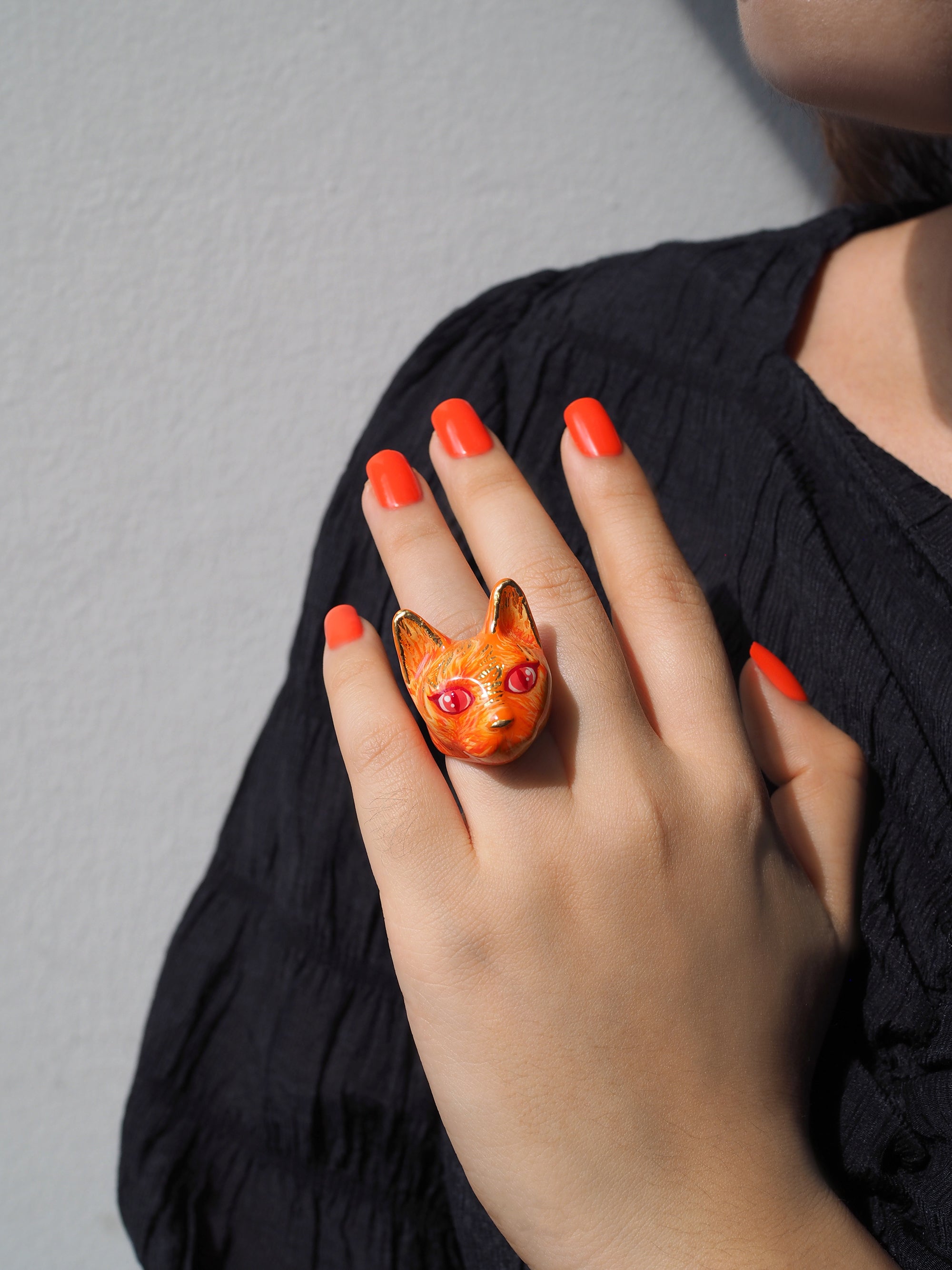 A vibrant orange cat ring with fiery details worn on a hand with bright red nails.