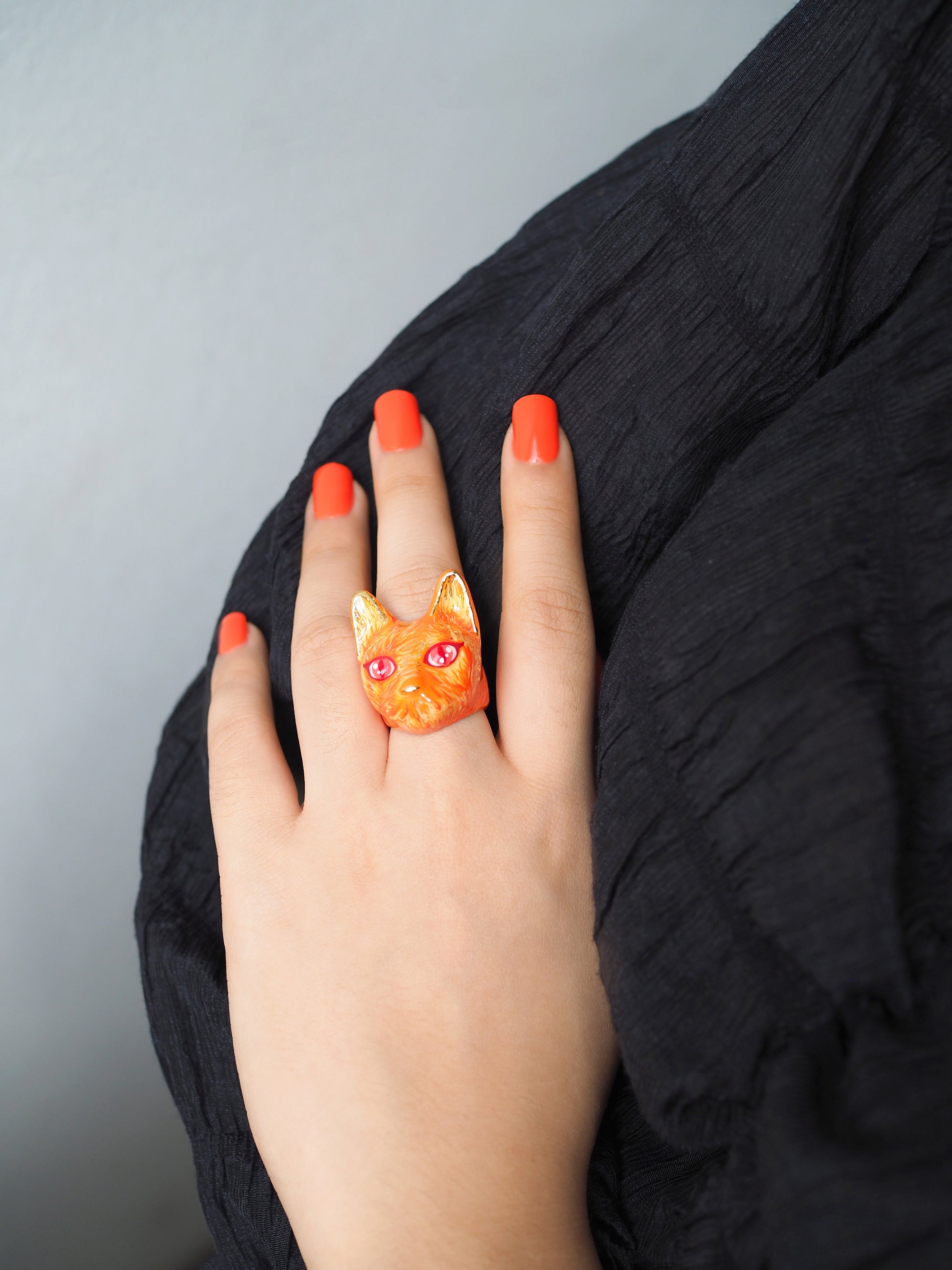 A vibrant orange cat ring with fiery details worn on a hand with bright red nails.