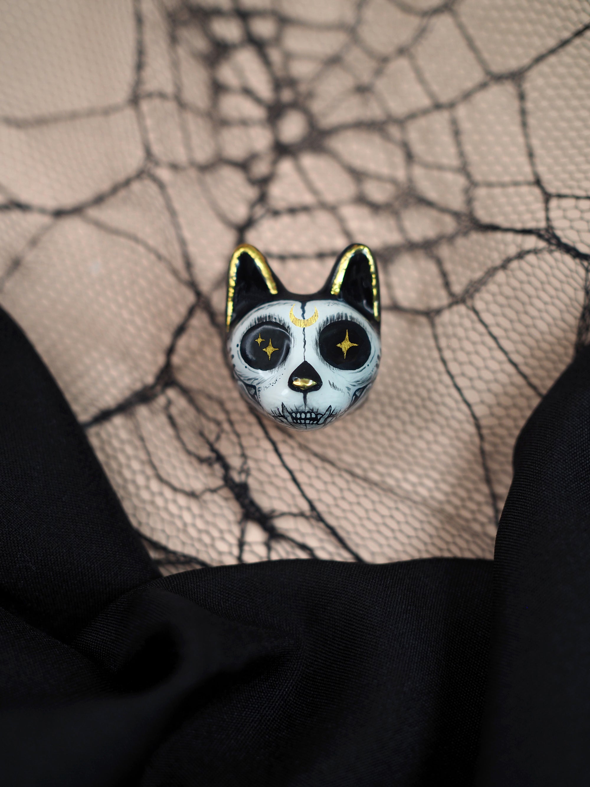 A halloween-themed black and white cat ring with skull motif placed on a decorative spider web and a black fabric.