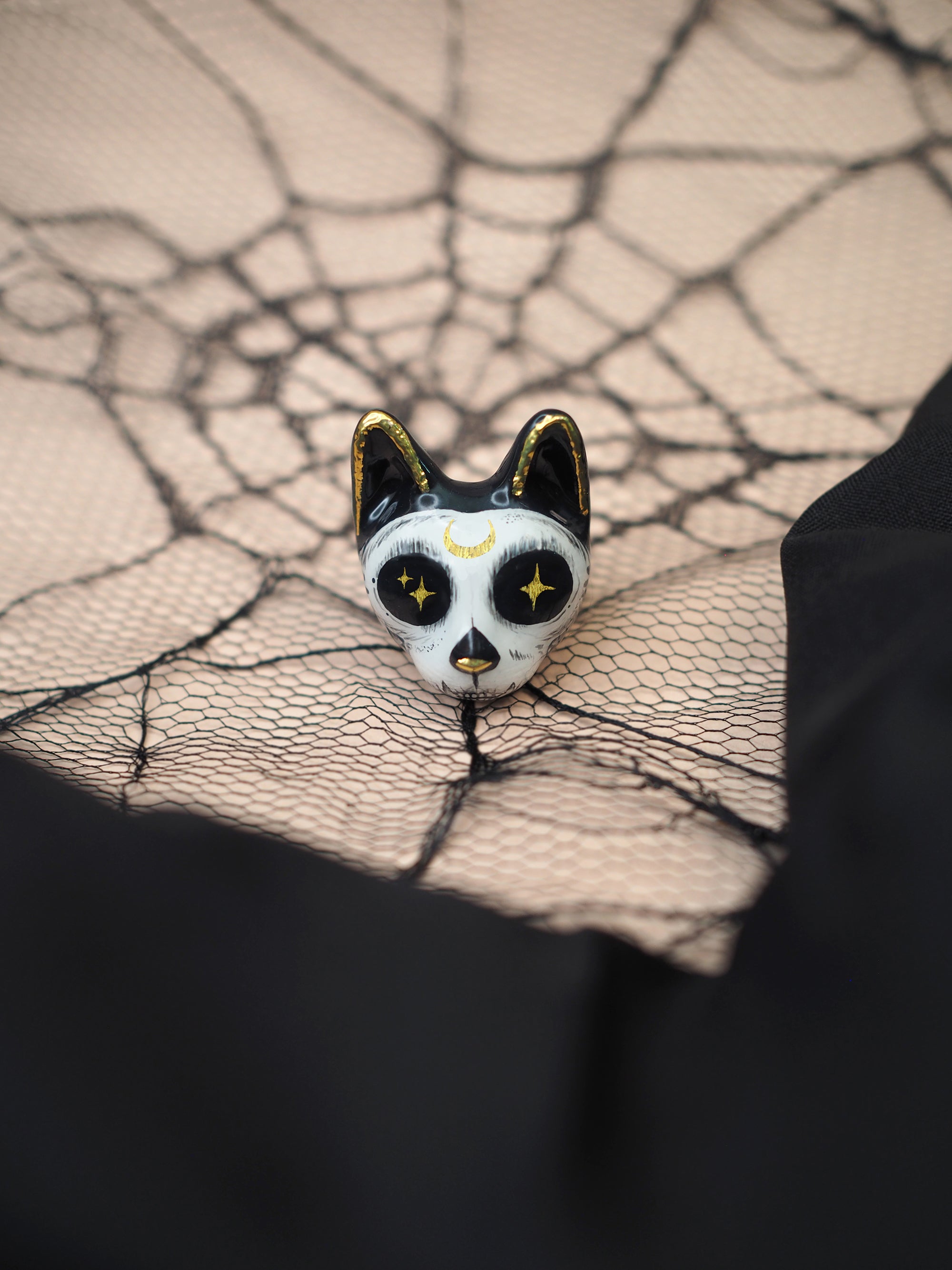 A halloween-themed black and white cat ring with skull motif placed on a decorative spider web and a black fabric.