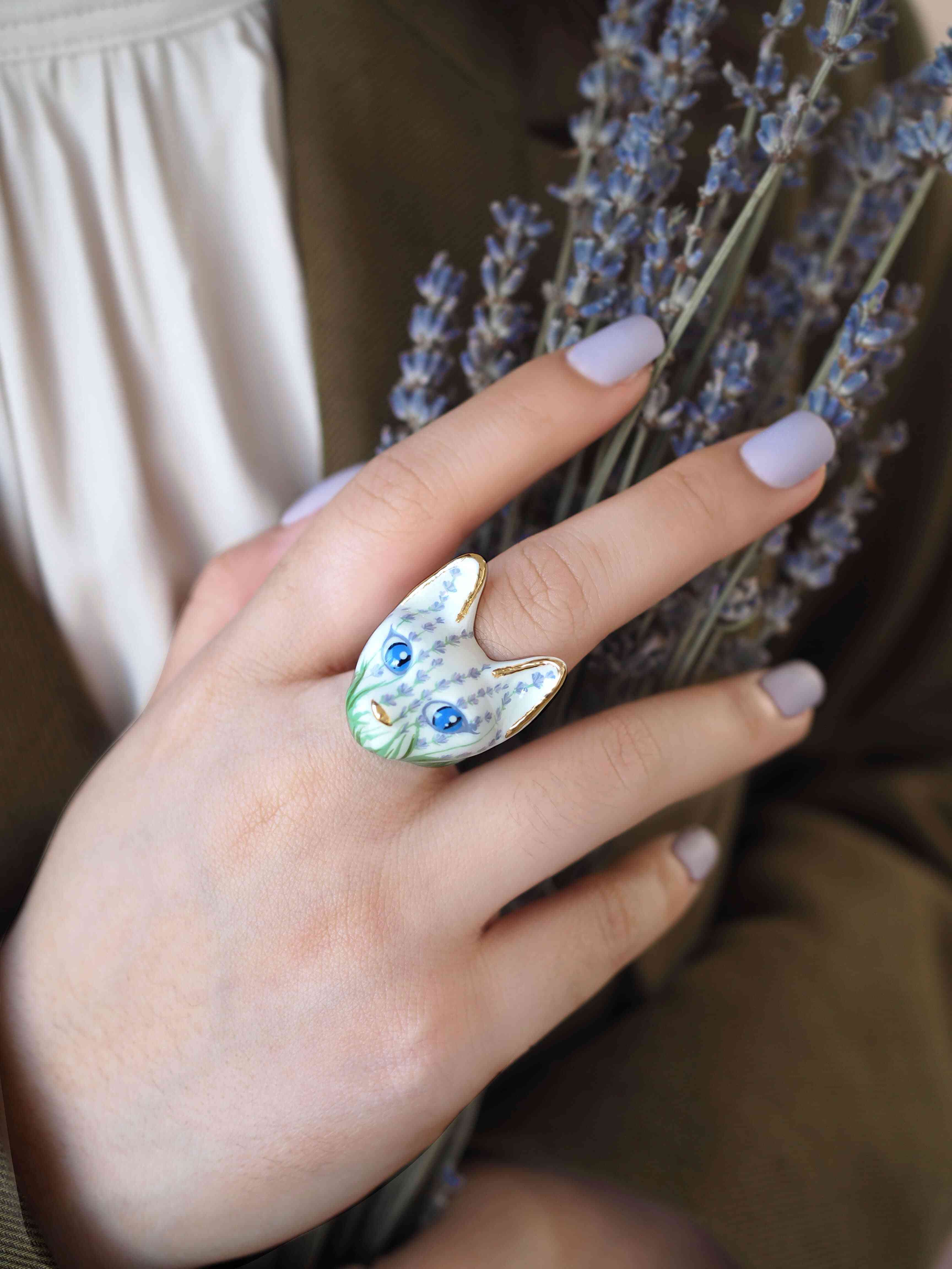 A hand adorned with a beautiful cat ring featuring lavender flowers pattern, holding a bundle of lavender flowers.