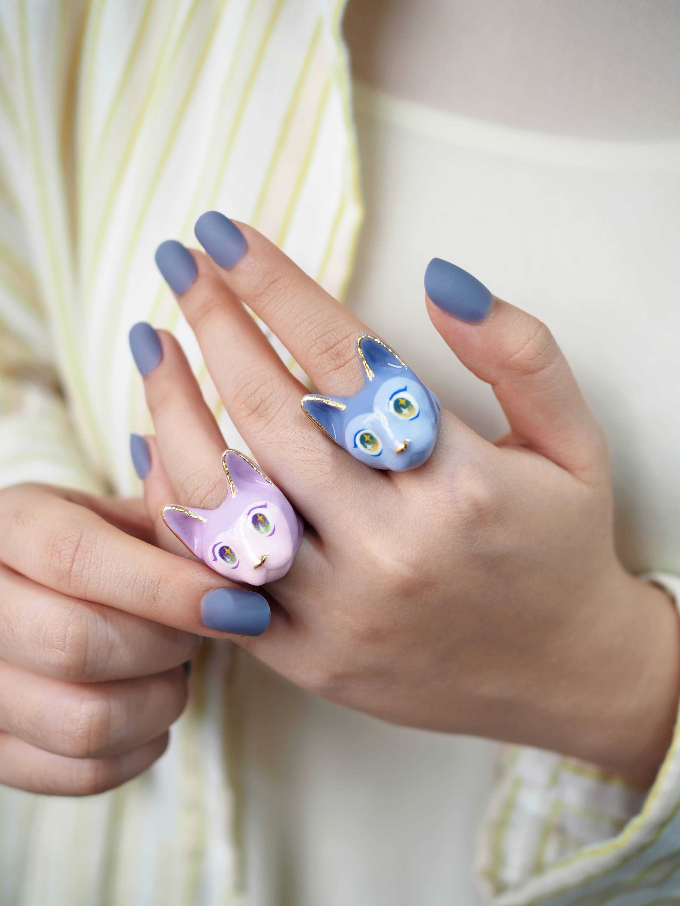 Two unique cat rings featuring a playful design and vibrant colors on a hand with purple nails.