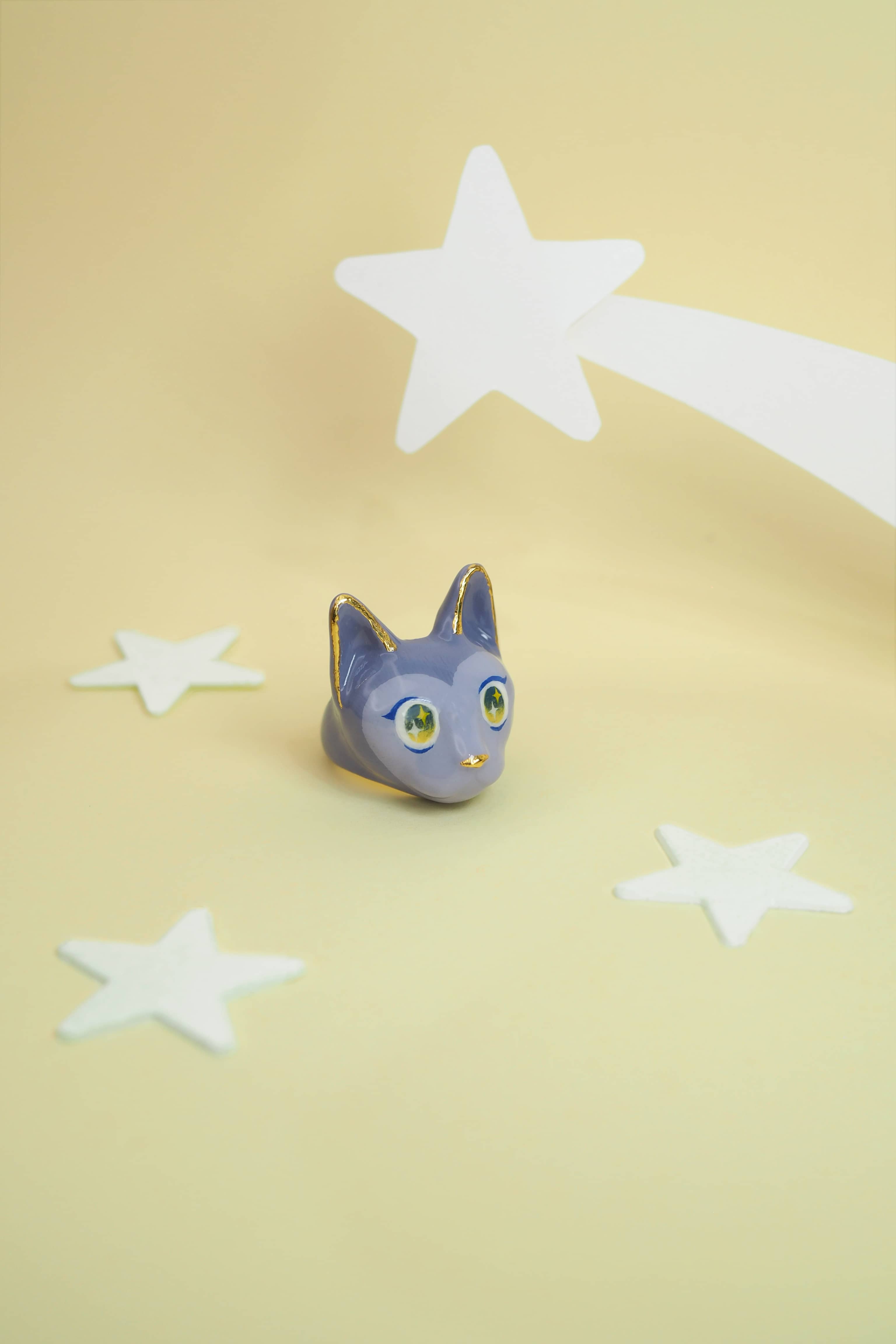 Whimsical cat ring featuring a playful design in purple hues with stars in the background, perfect for art collectors.