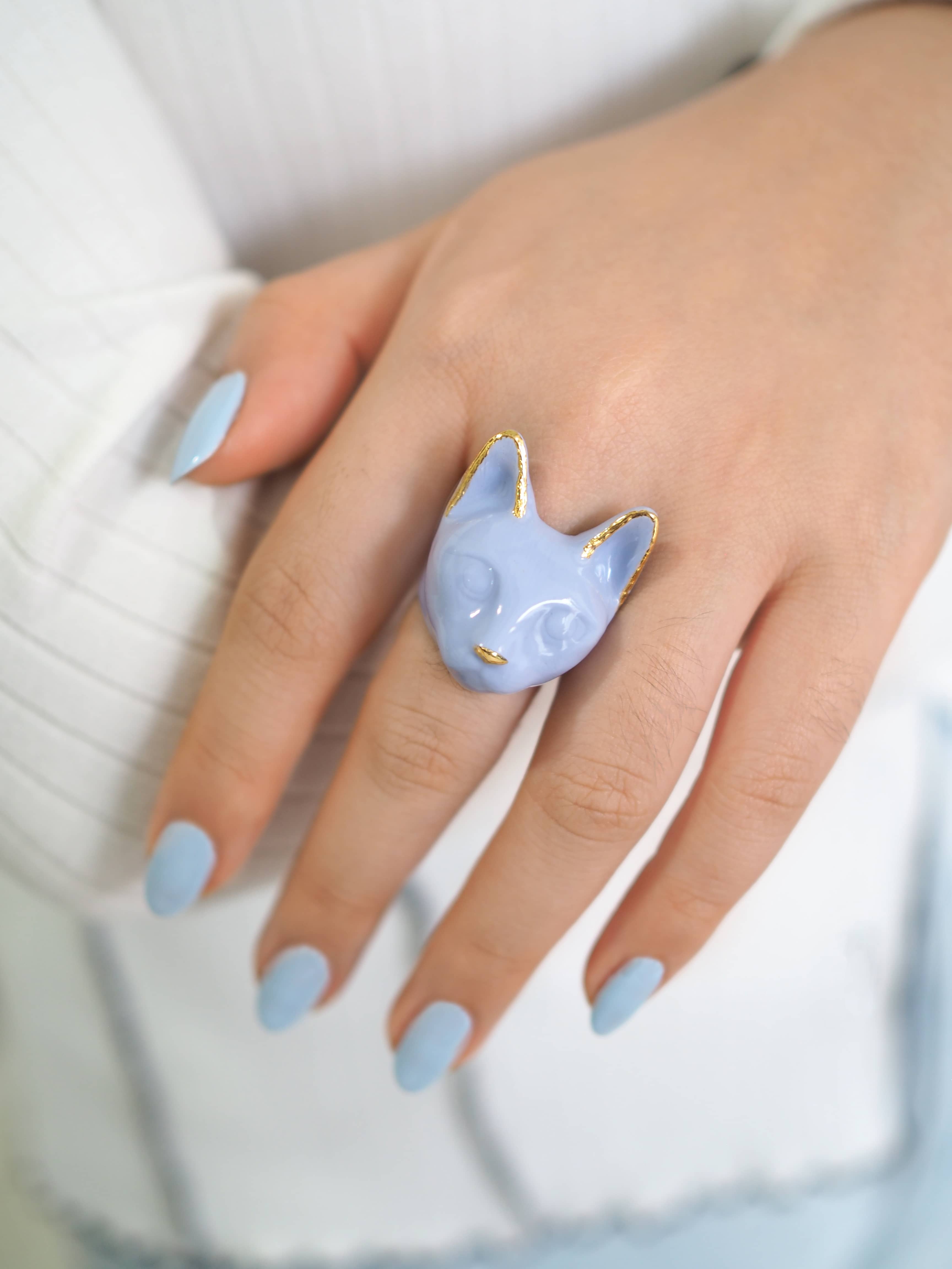 Close up of a cat ring featuring a soft lavender color worn on a person's hand.