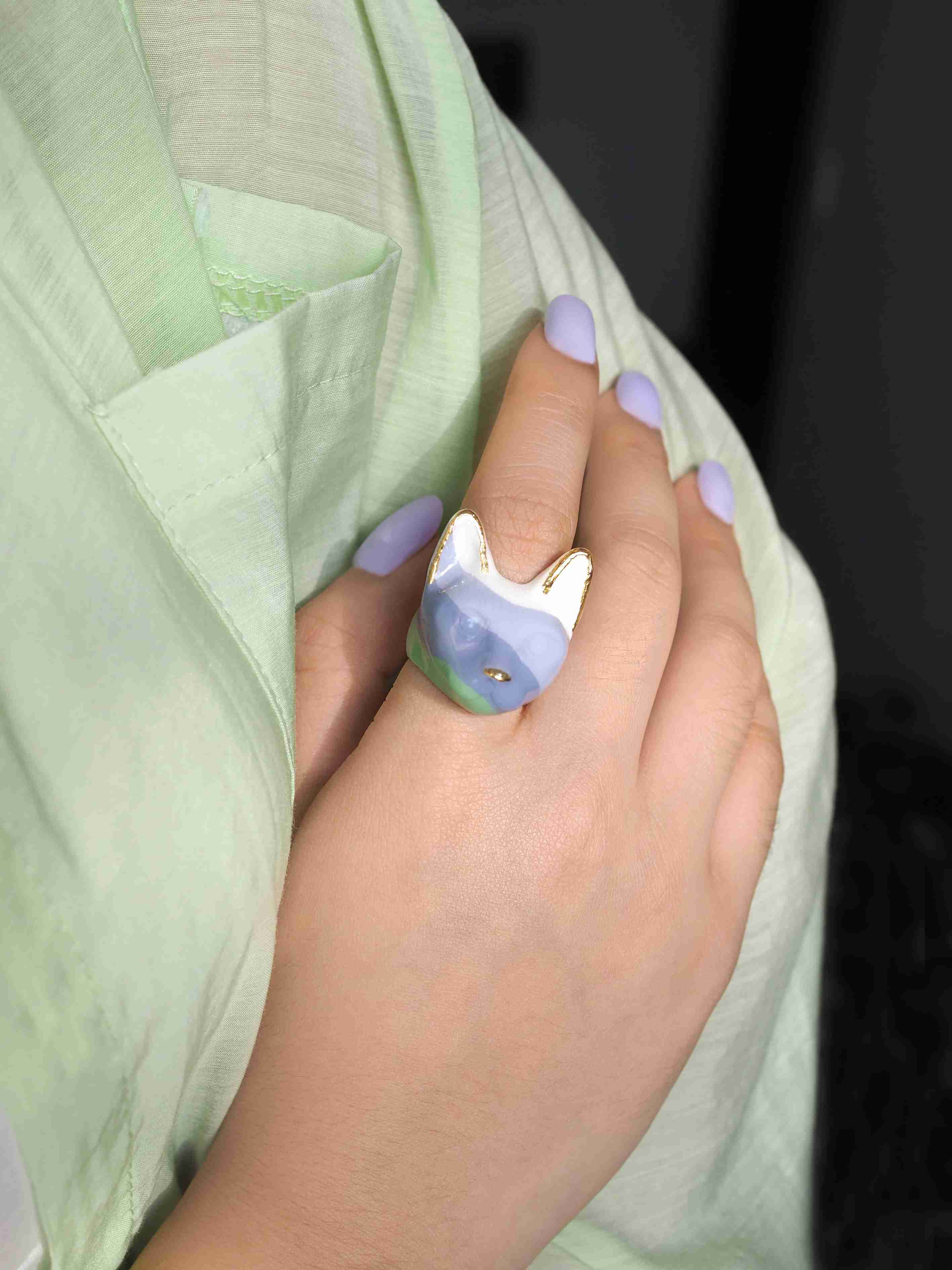 Close up of a hand adorned with unique cat ring in lavender, green and white.