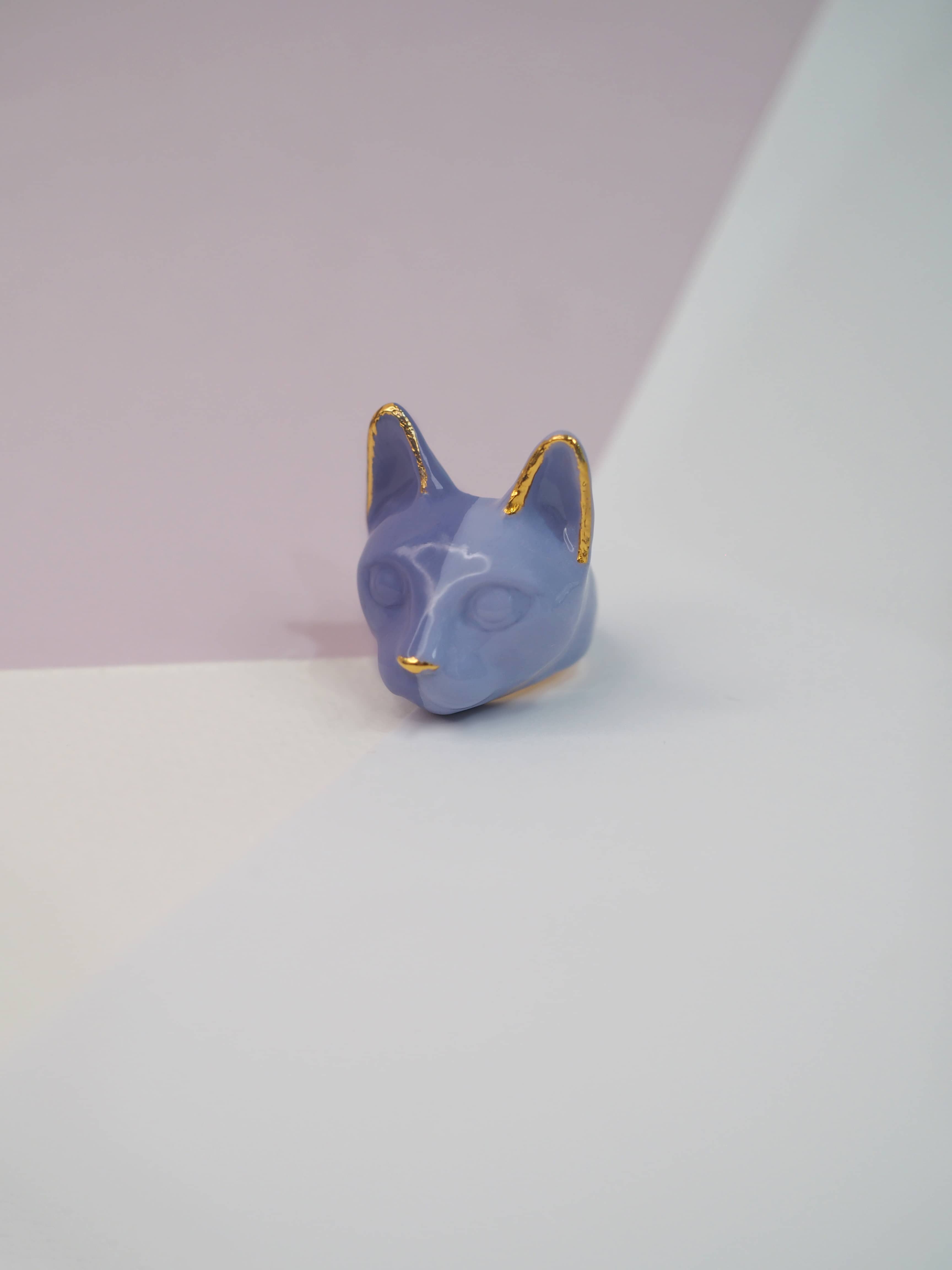 Whimsical purple cat ring design placed on pastel background.