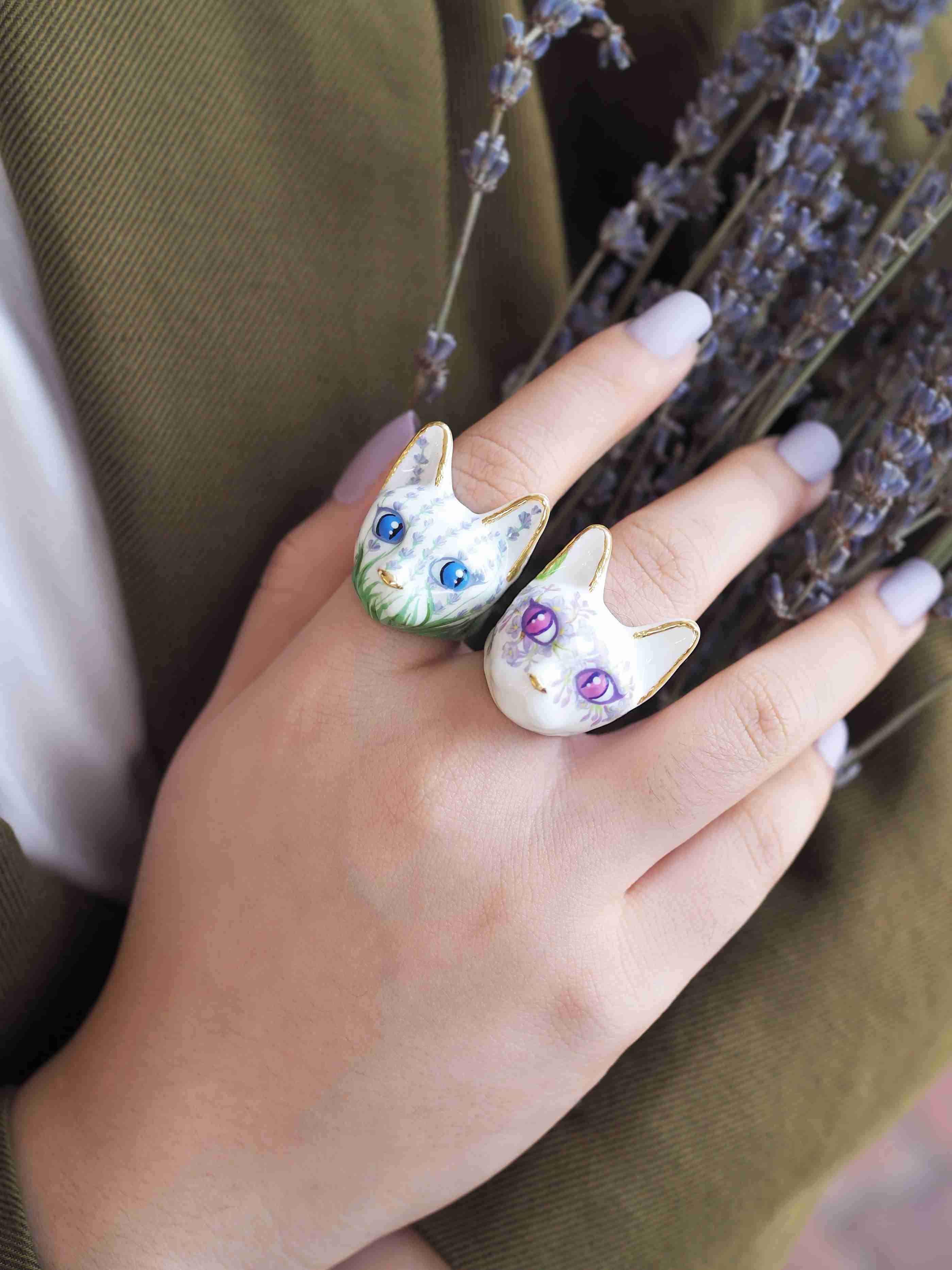 A hand adorned with two hand-painted cat rings featuring lavender flowers pattern and lilac flowers pattern, holding a bundle of lavender flowers.